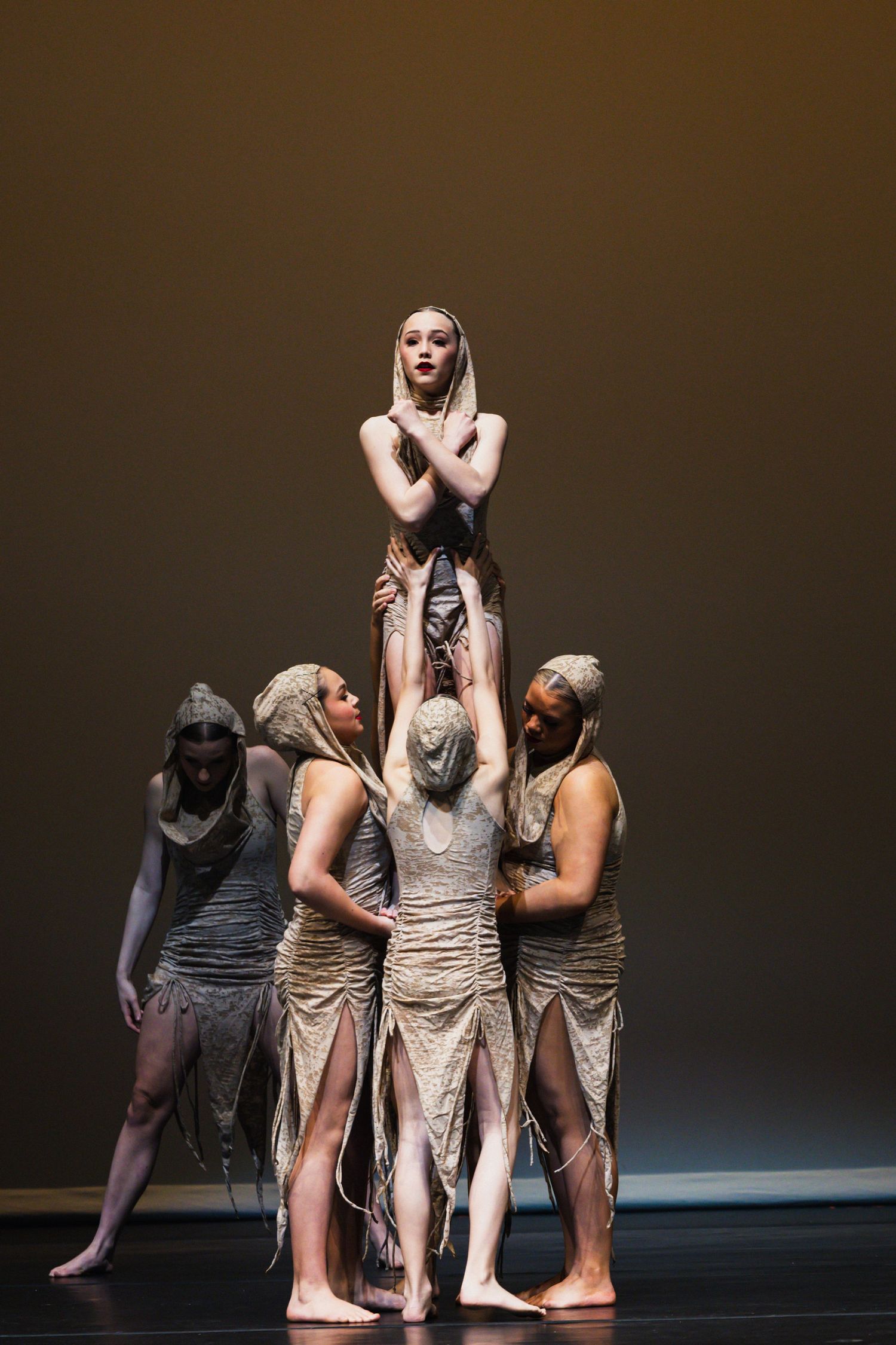 Contemporary dancers in neutral tones perform an emotional group piece on a dark stage.