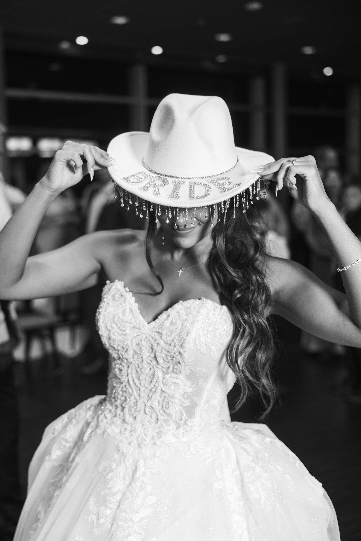 Bride in lace wedding gown wearing a rhinestone BRIDE cowboy hat at wedding reception.