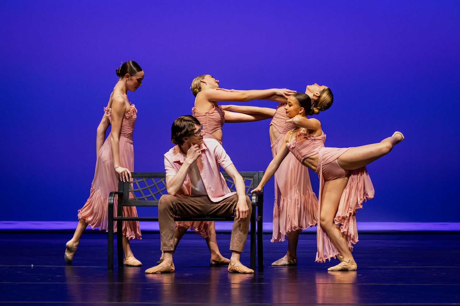 Dancers in beige costumes perform a synchronized modern dance routine against a deep blue stage backdrop.