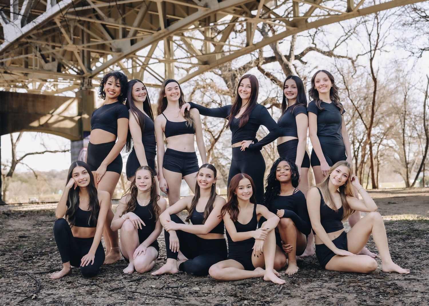 A group in black outfits poses together outdoors for a dance team photo shoot.