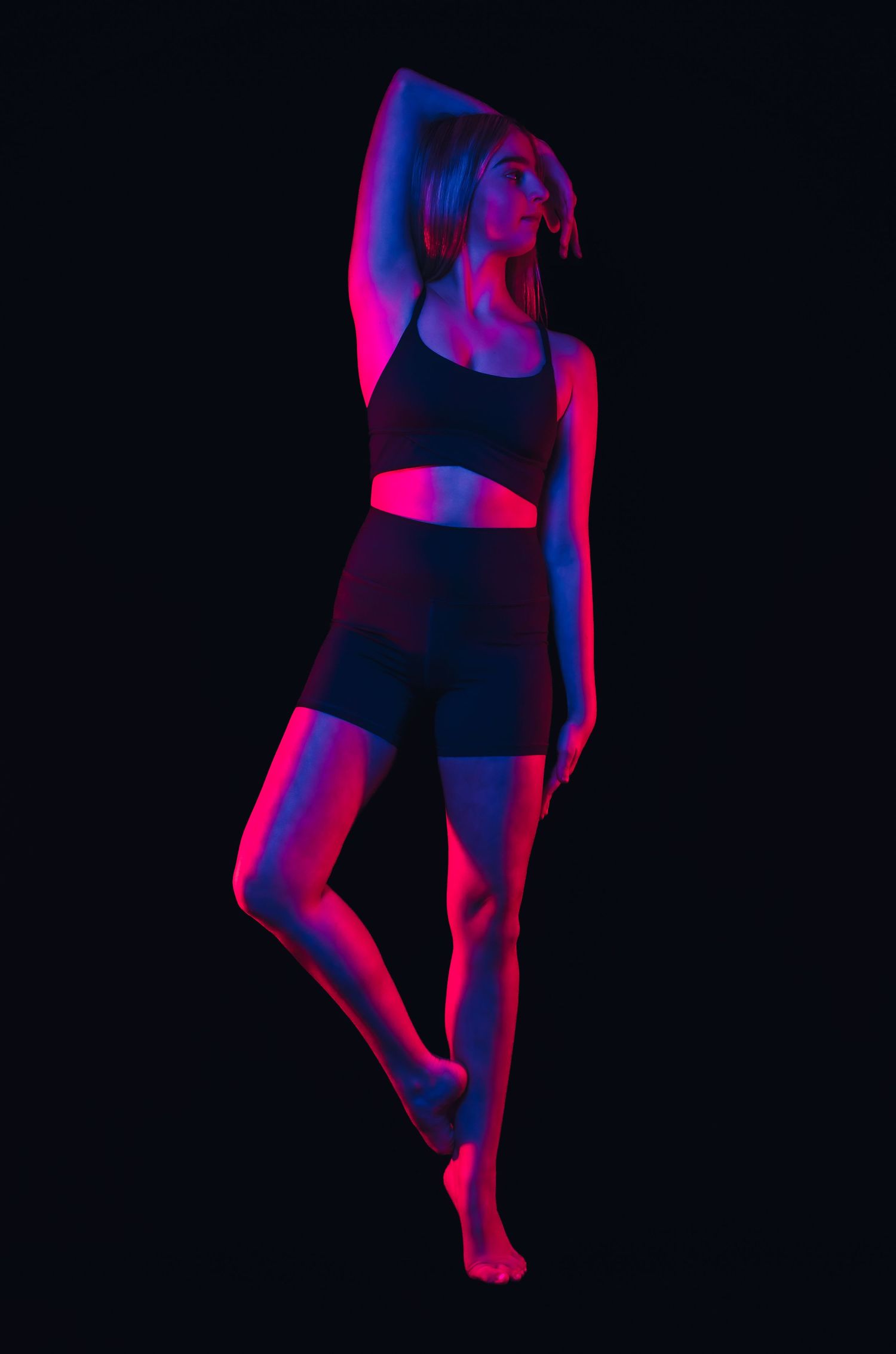 Athletic figure in black workout attire poses against dark background with dramatic red and blue lighting effects.