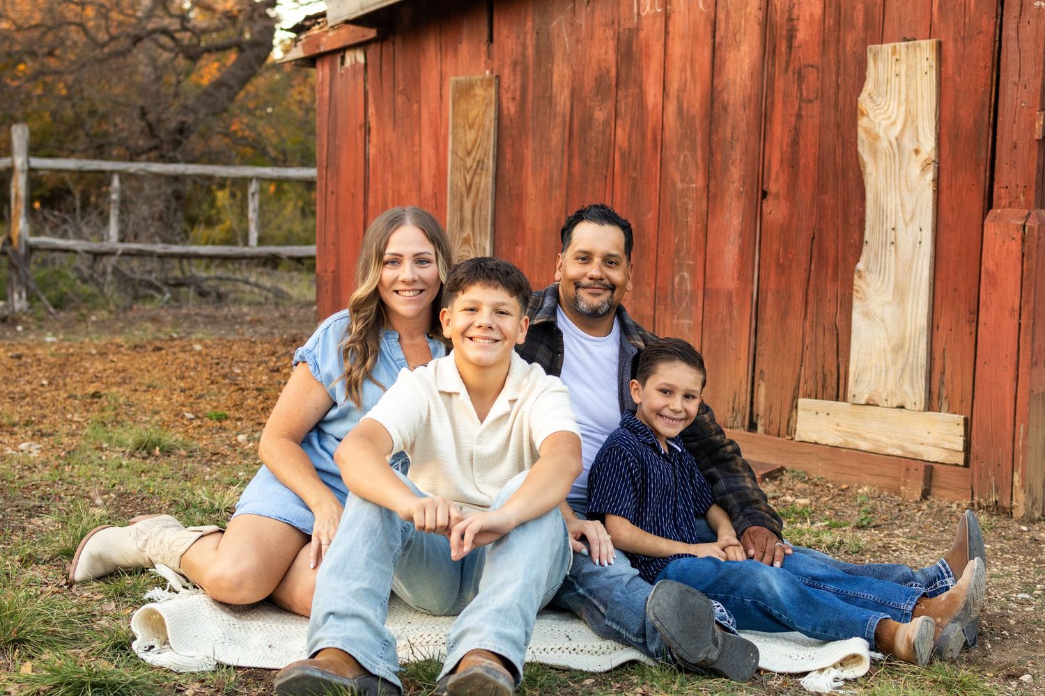 Family portrait session against weathered red barn in natural outdoor setting.