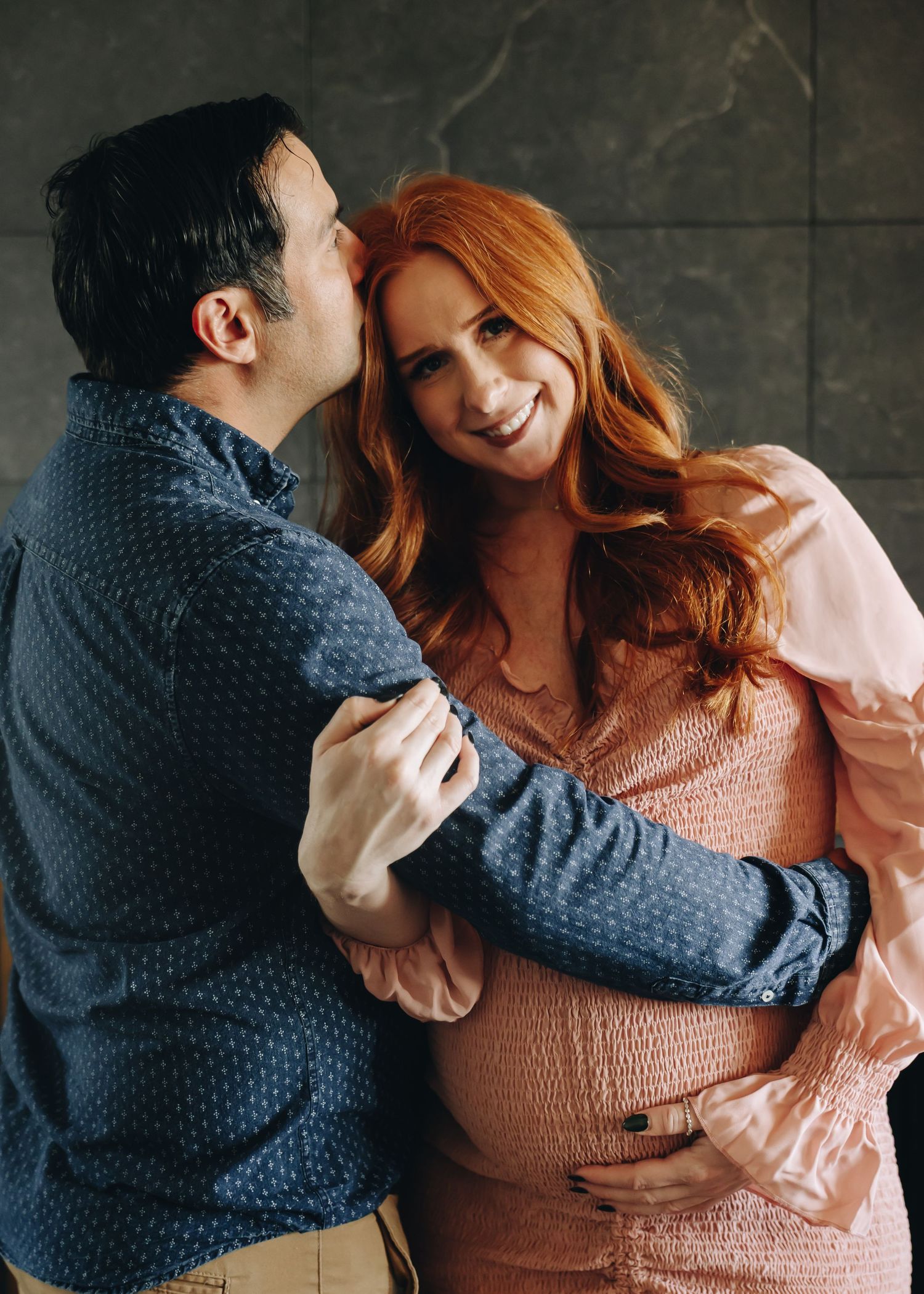 Romantic couple embracing in cozy sweaters against grey wall.
