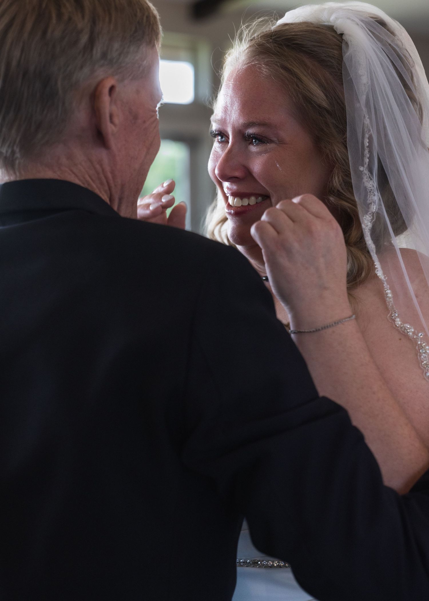 Emotional bride smiling tearfully as older man gently touches her face during a heartfelt wedding ceremony moment.