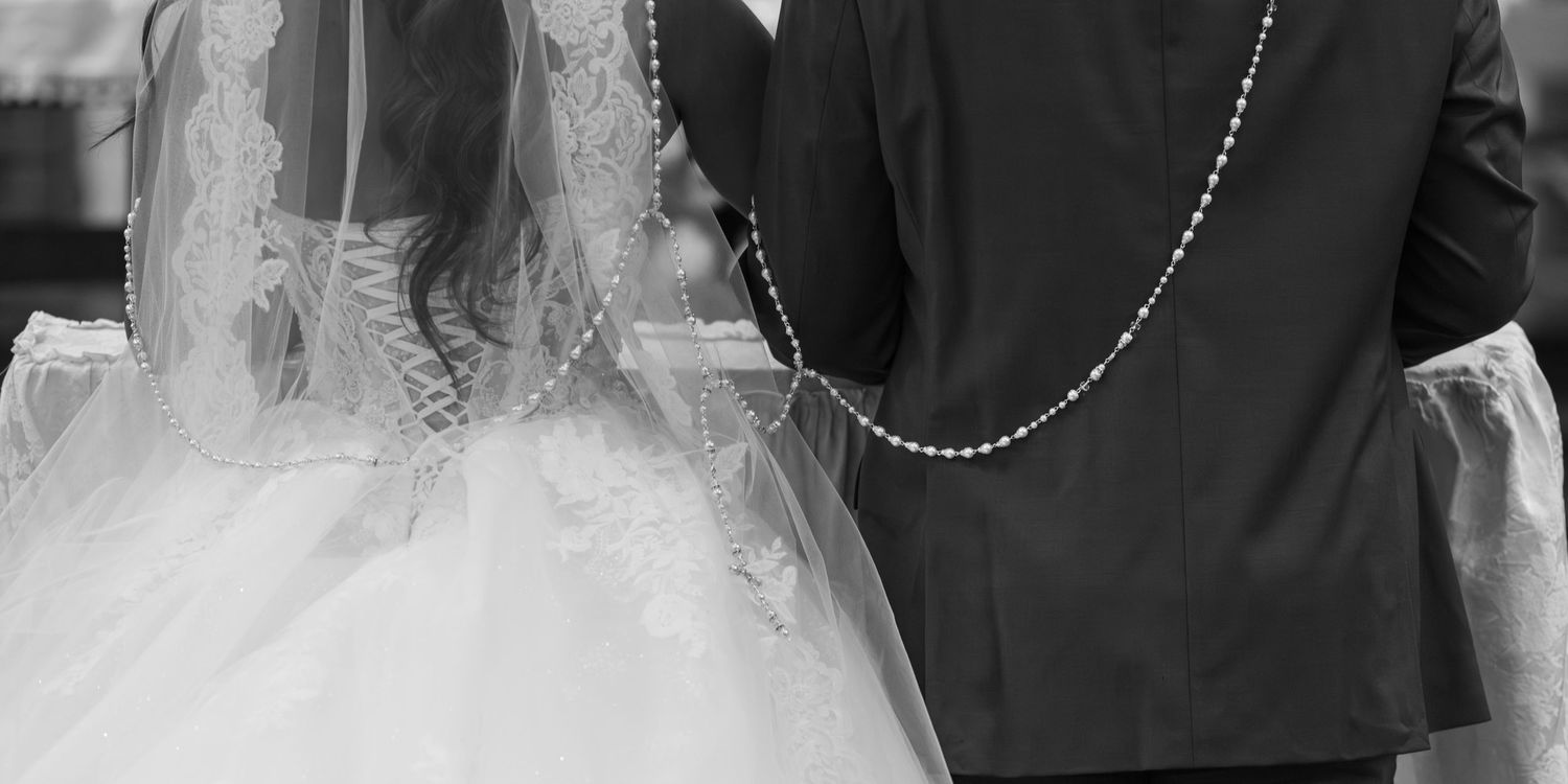 Black and white photo of bride and groom holding pearl rosary beads at wedding ceremony.