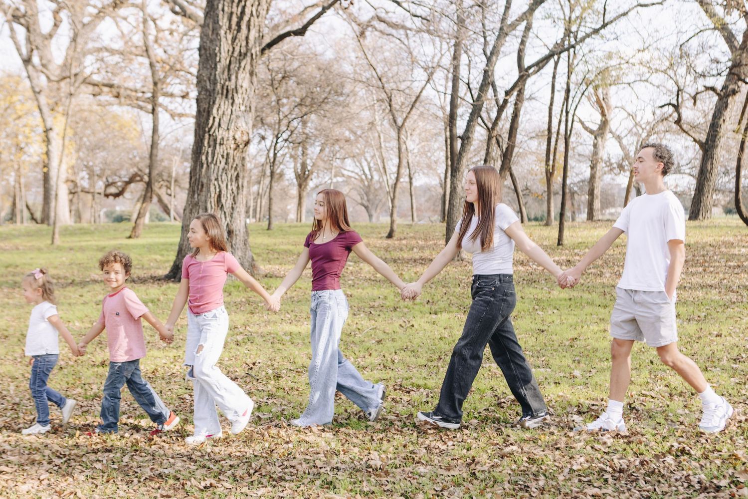 A group of children walk in a line through an autumn park during an outdoor activity.