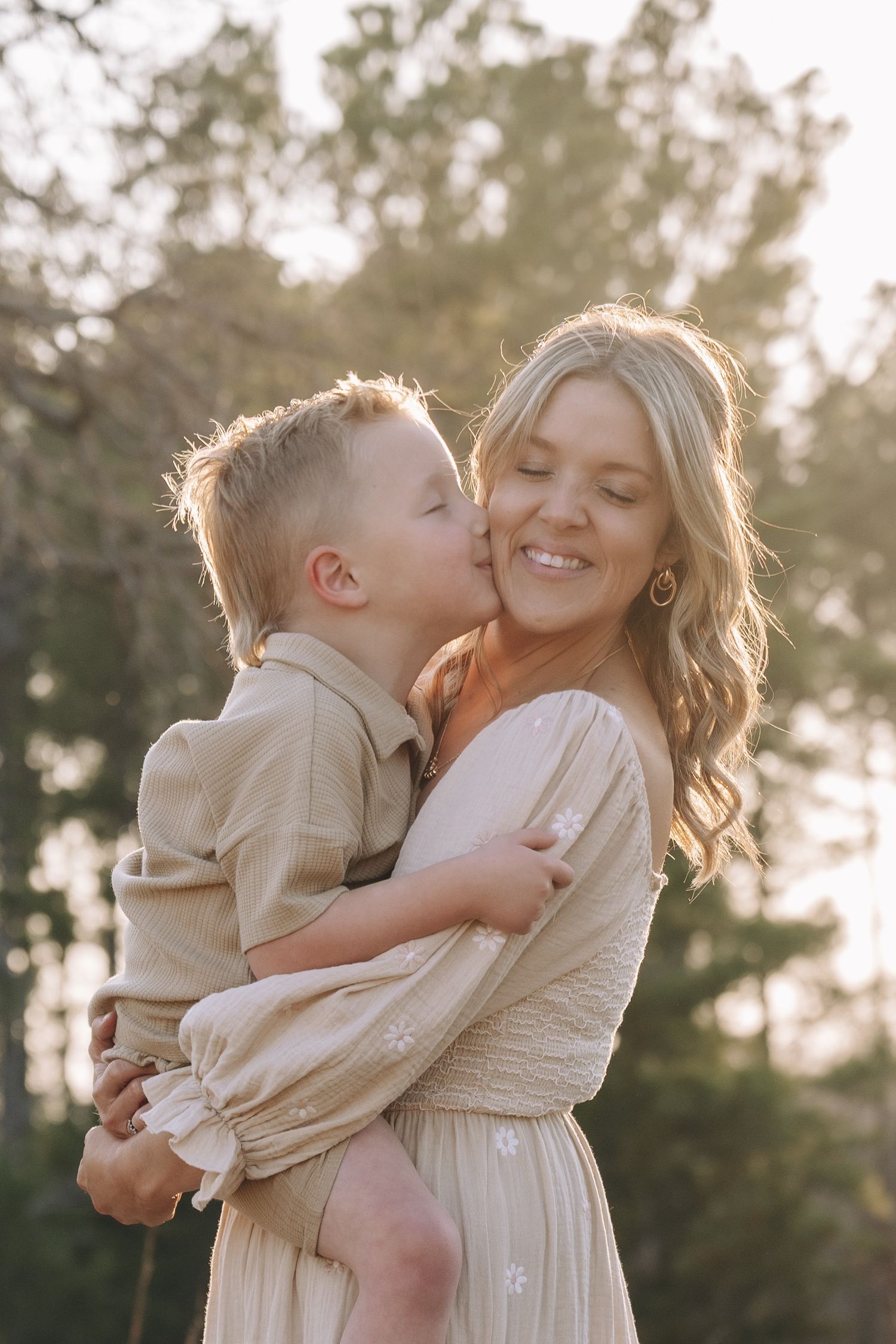 A tender moment captured at sunset as a young child in beige embraces someone wearing a cream-colored dress.