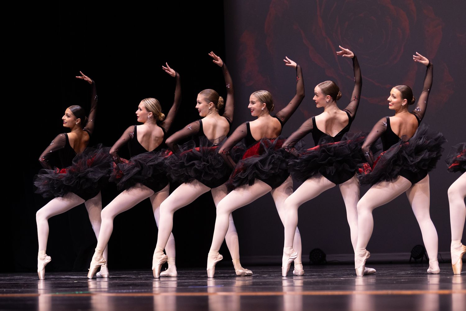 Ballet dancers in black tutus perform on stage in perfect unison during a classical ballet performance.