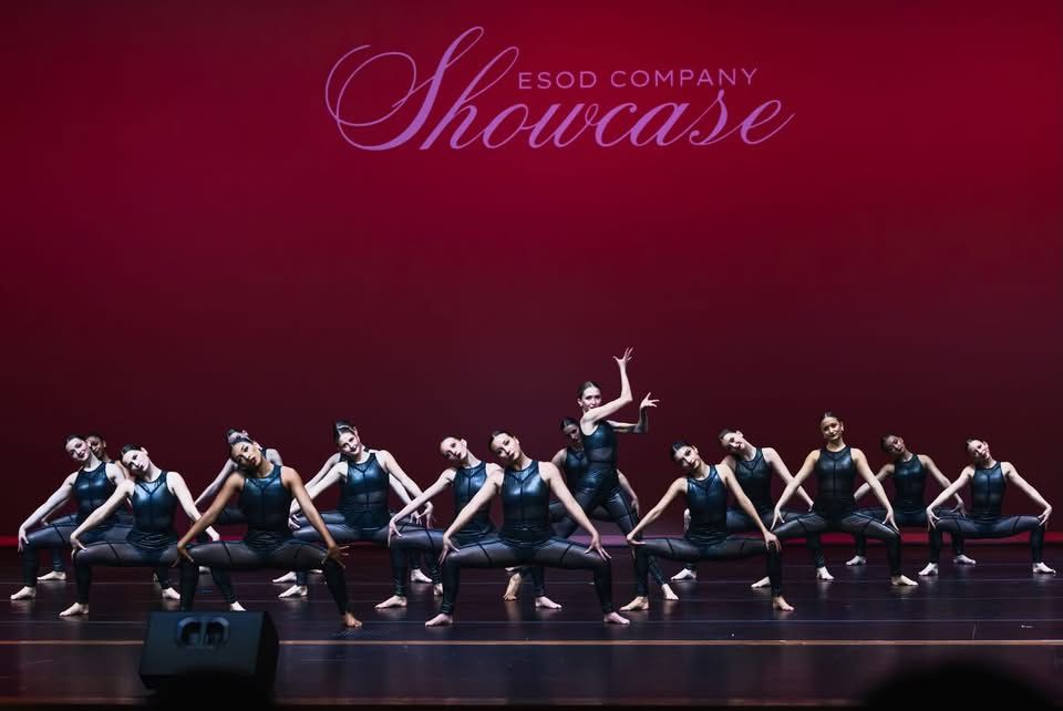 Ballet dancers perform in a dramatic sequence on stage with red lighting and coordinated movements in perfect unison.