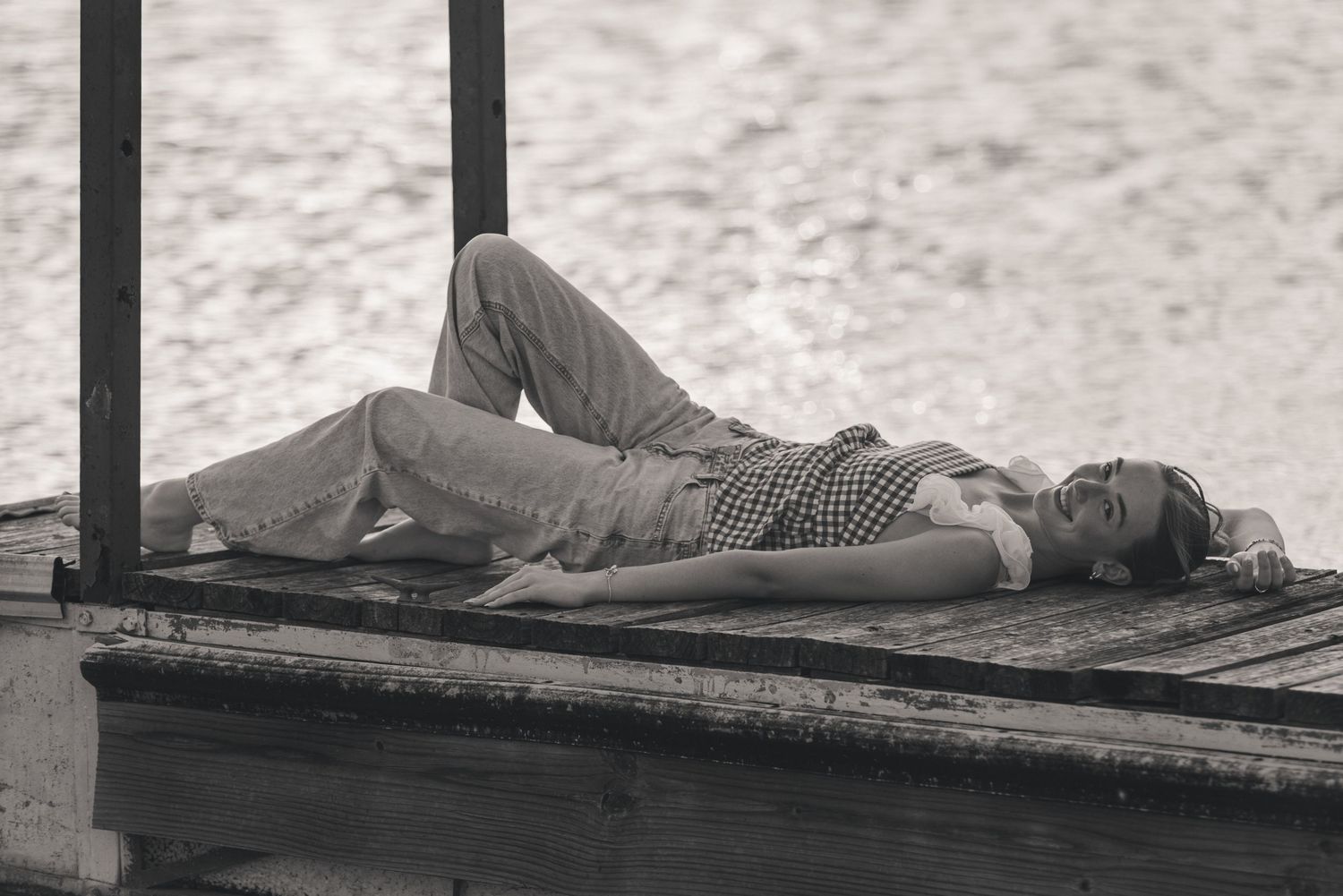 Black and white photo of a woman relaxing on a wooden dock by the water.