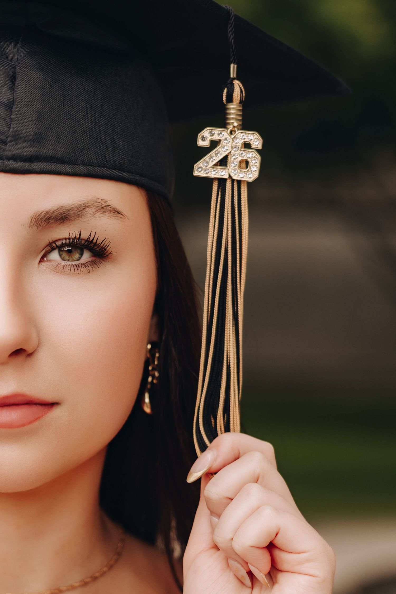 Young woman in black graduation cap with gold '26' tassel charm, close-up portrait for class of 2026.