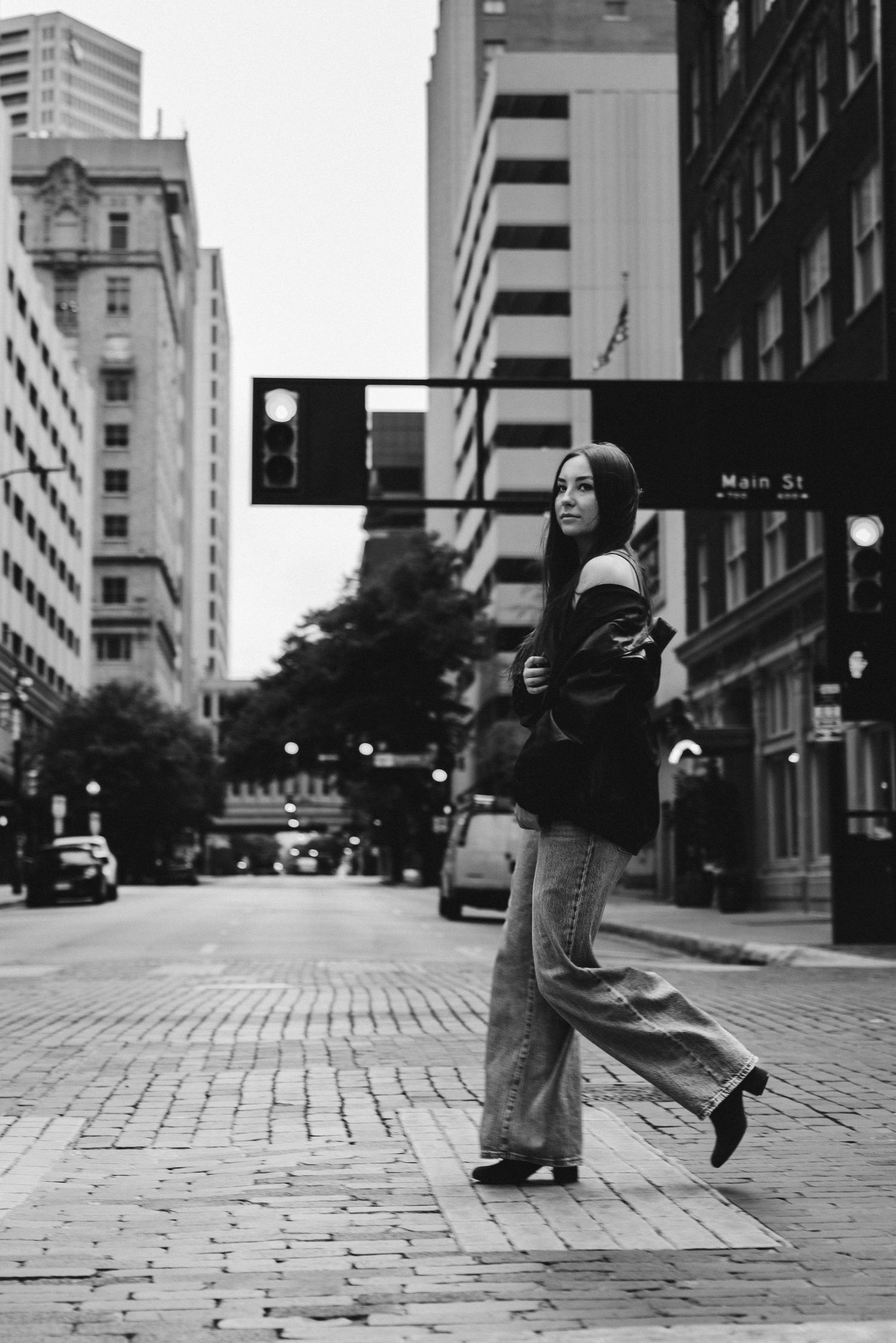 Black and white photo of a woman posing on a brick crosswalk on Main St in an urban downtown setting.