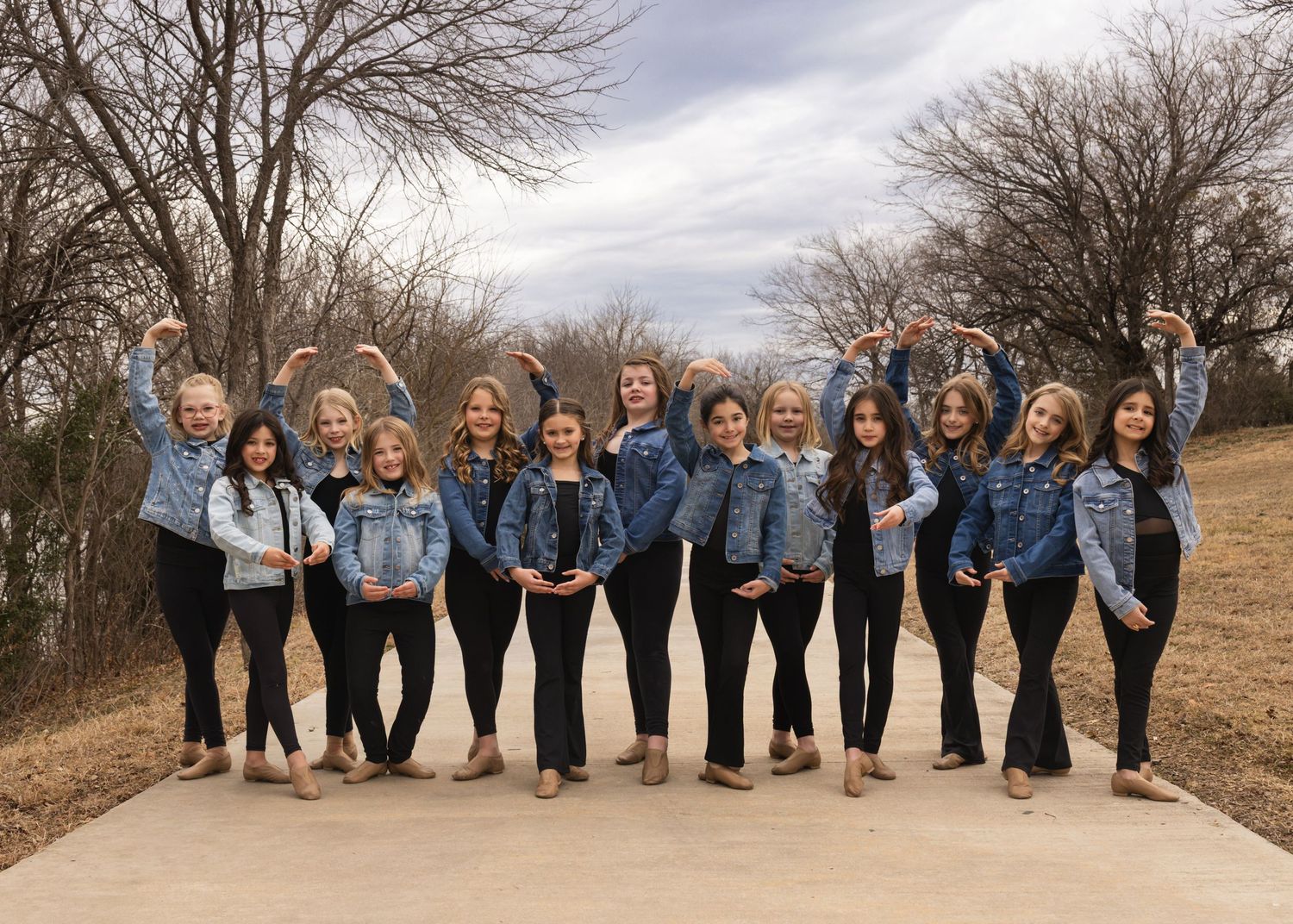 A group wearing matching denim jackets poses together on a path with bare trees in the background.