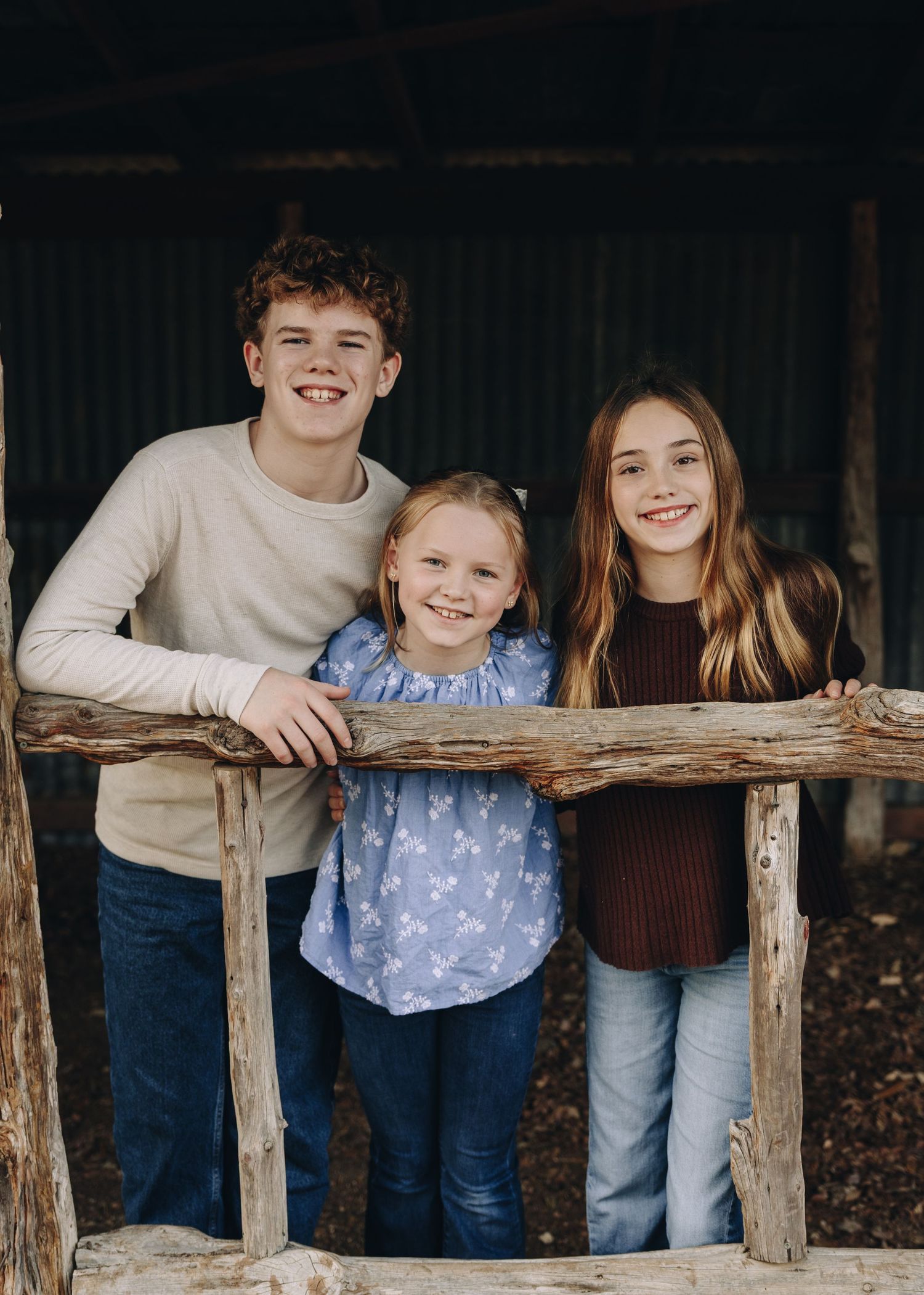 A group in casual attire leans against a rustic wooden fence while posing together for a casual outdoor portrait.