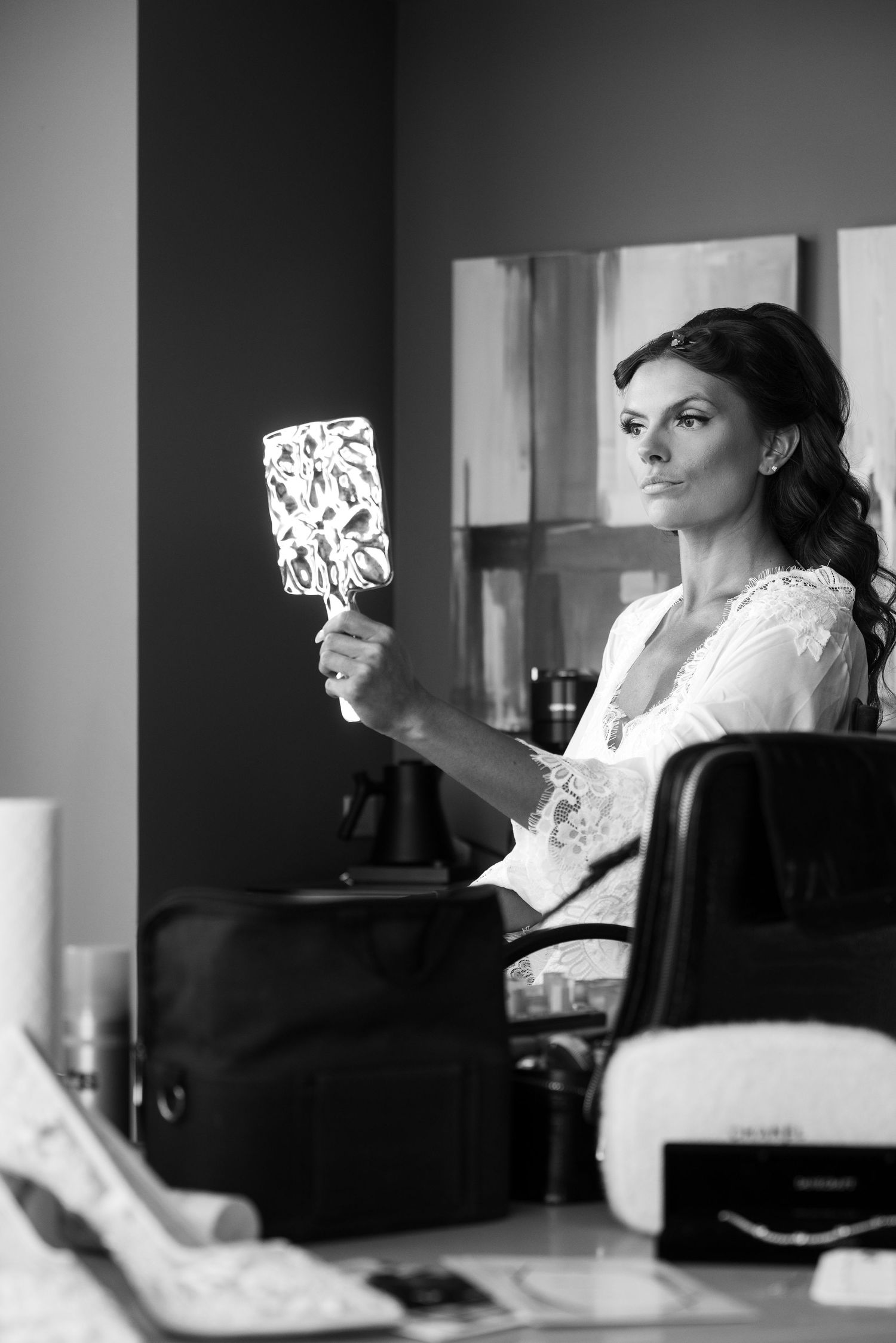 Black and white photo of a bride holding a mirror at a salon while getting ready for her wedding day.