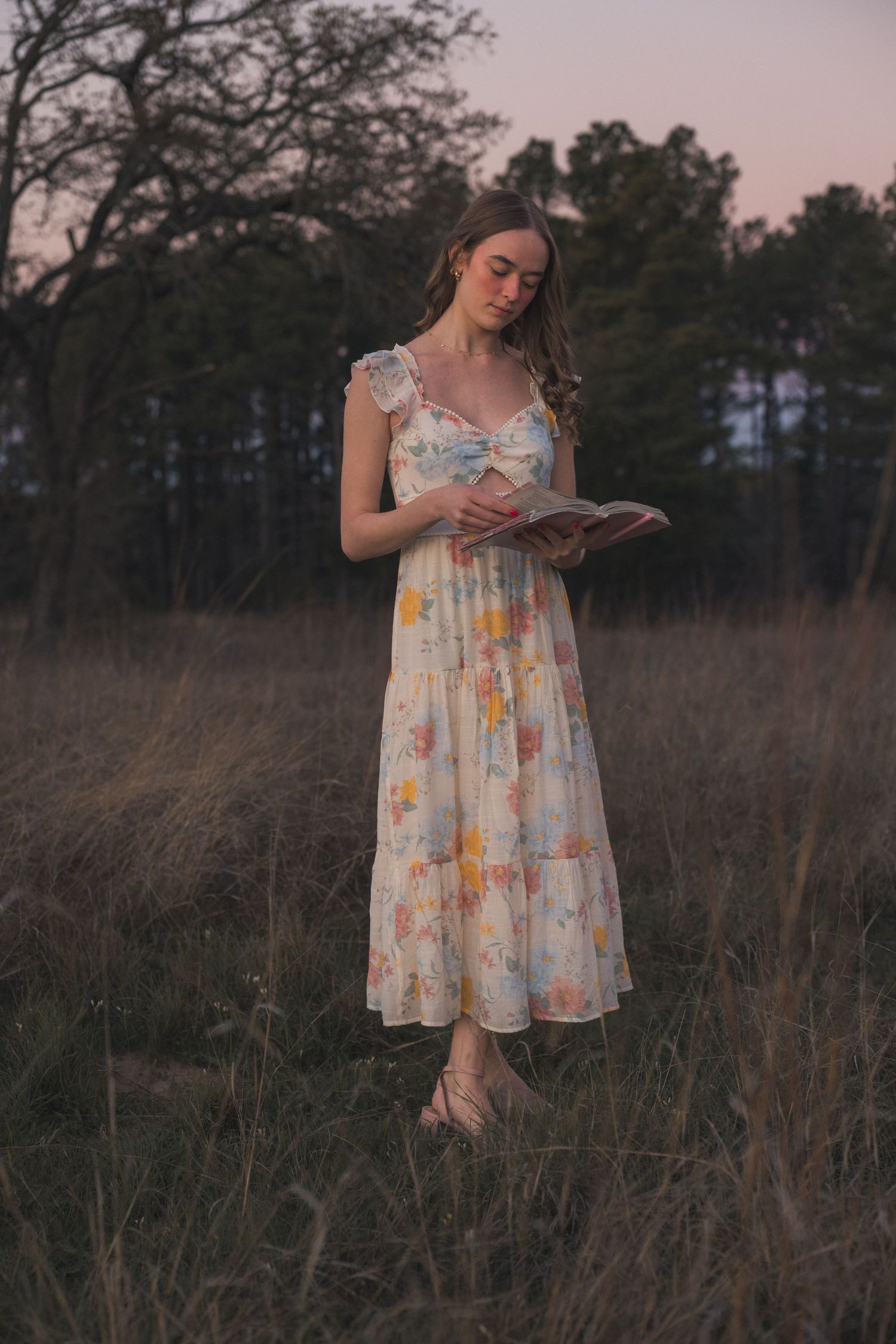 A dreamy portrait of someone in a floral dress reading a book in a golden field at dusk.