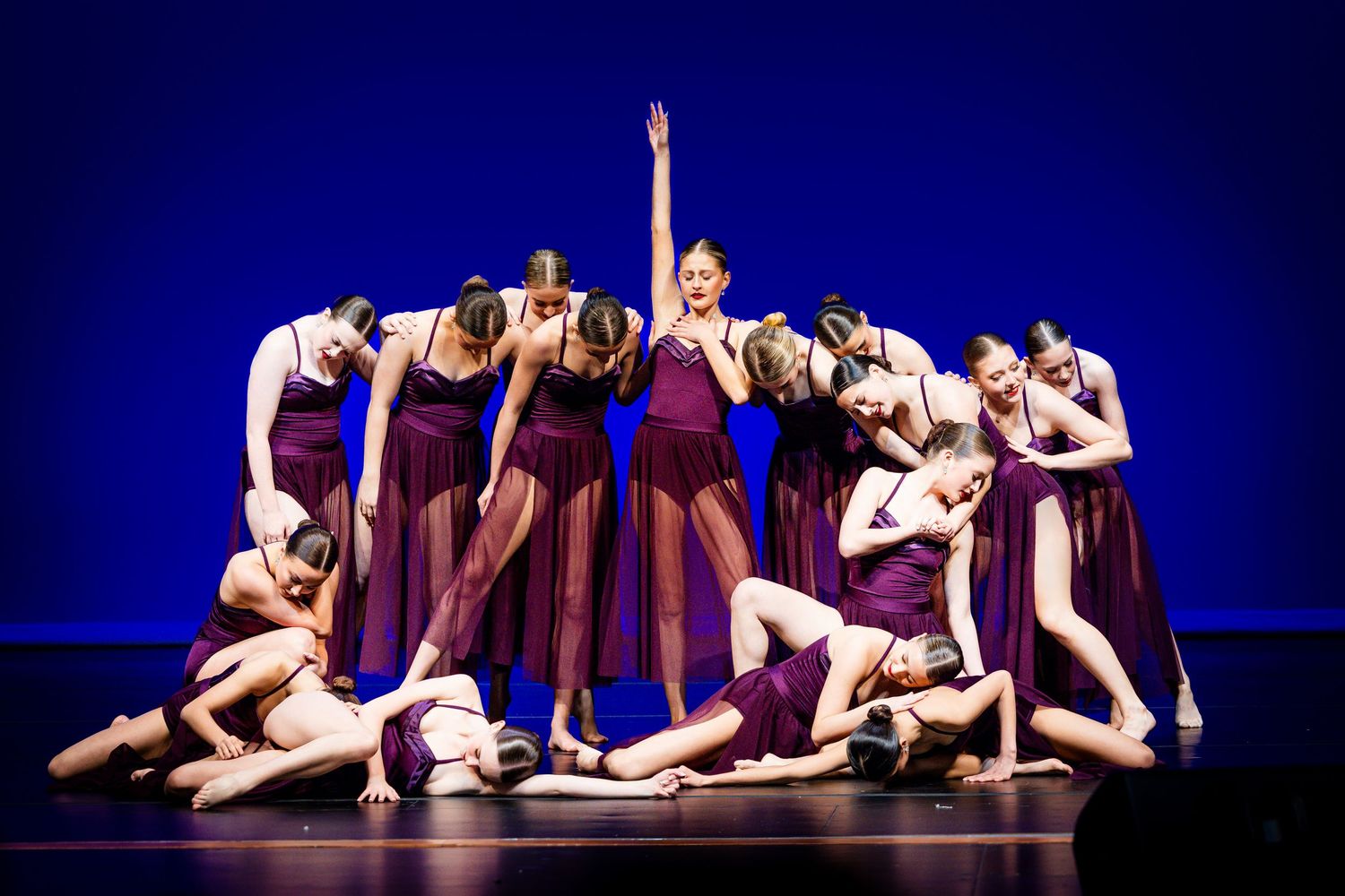 Dancers in elegant poses perform on a dark stage with dramatic blue lighting during a contemporary dance performance.