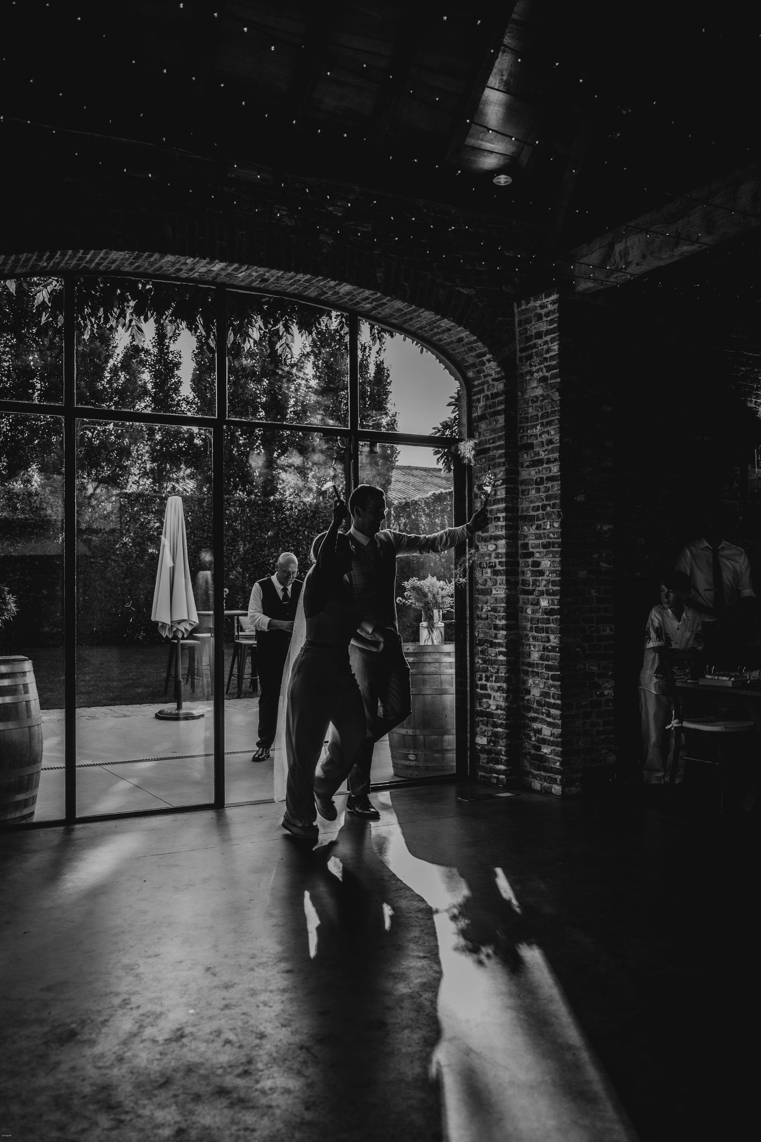 Silhouetted figures in a brick-walled venue with dramatic backlighting.