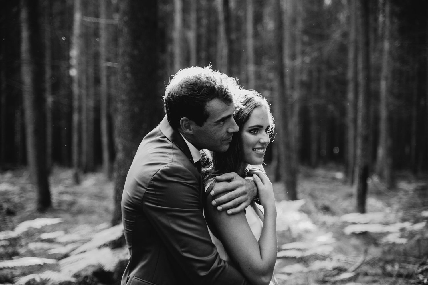 Black and white photo of couple embracing in forest setting.