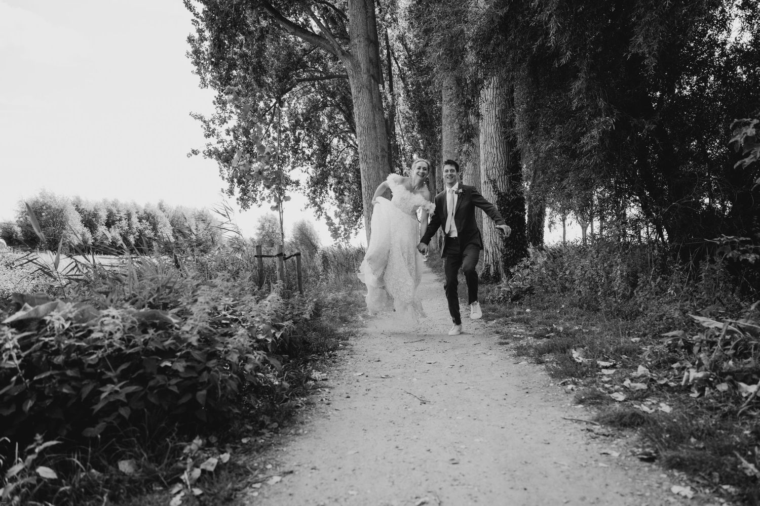 Black and white photo of a couple walking down a tree-lined path.