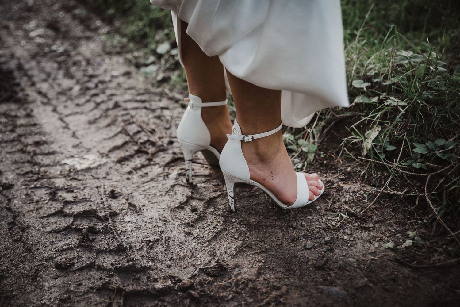 Close-up of bride's feet in white shoes walking on forest ground.