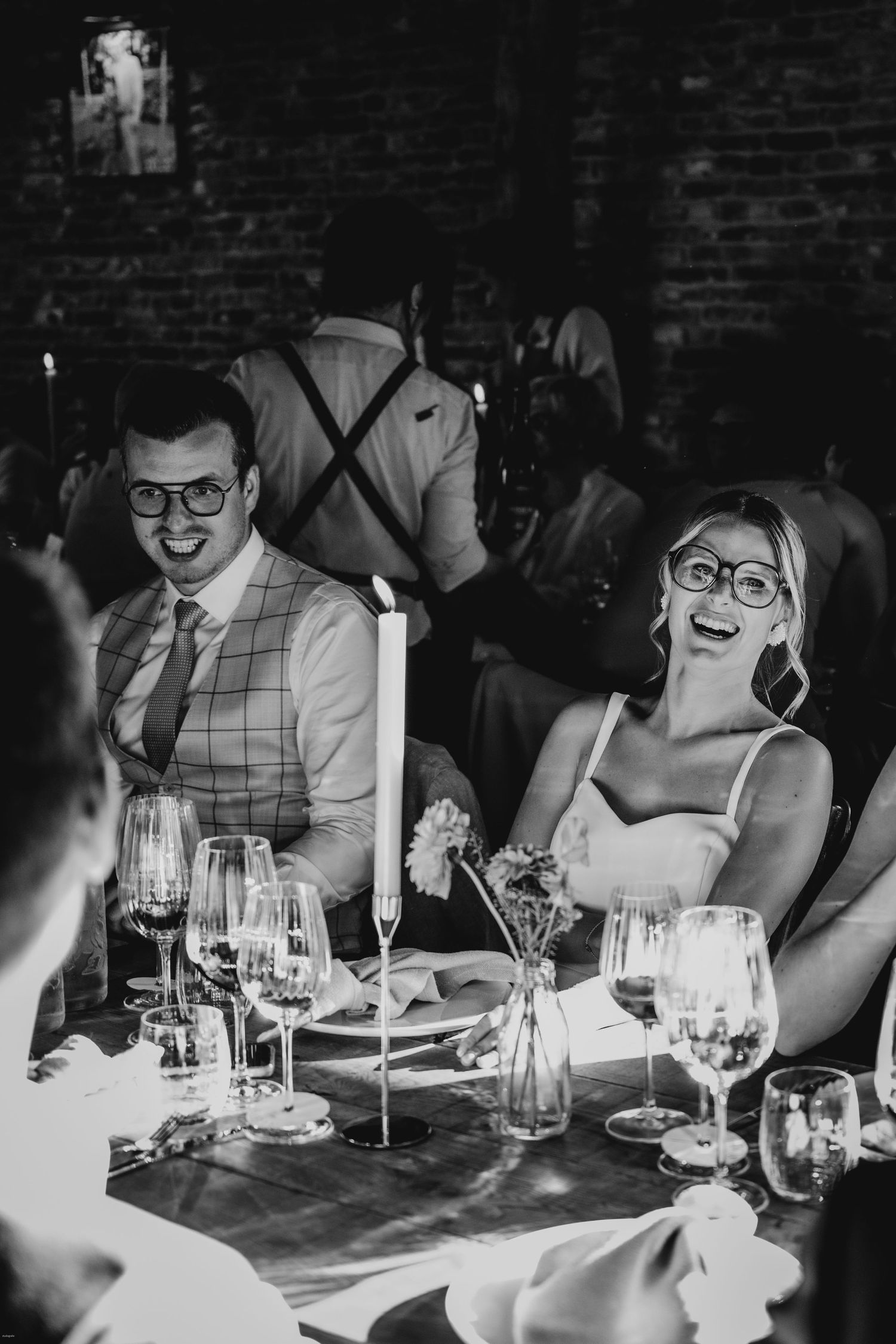 Black and white photo of guests dining at an intimate wedding reception with wine glasses.