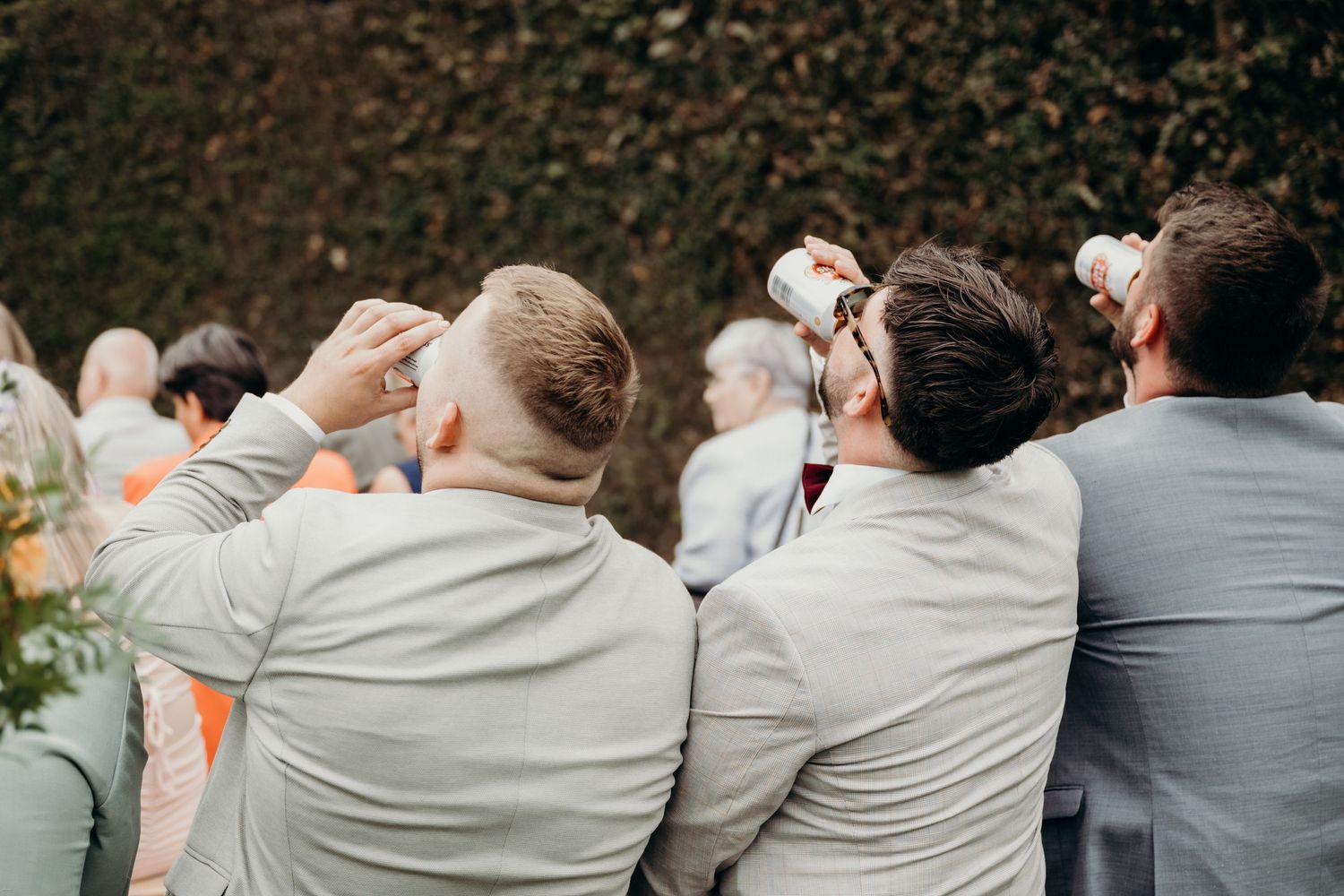 Row of groomsmen in gray suits shown from behind with arms around each other.