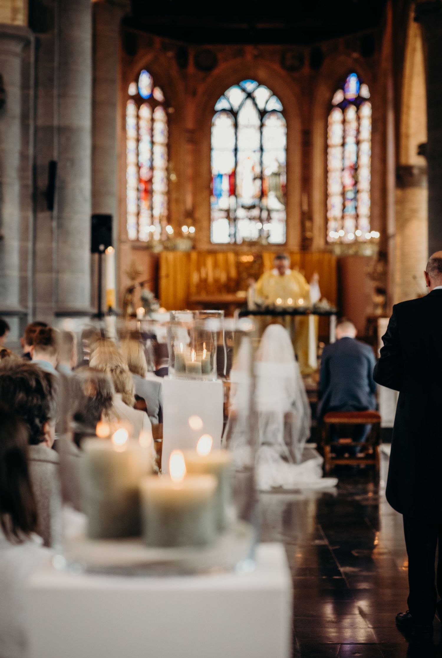 Church interior with stained glass windows and glowing candles set up for a wedding ceremony.