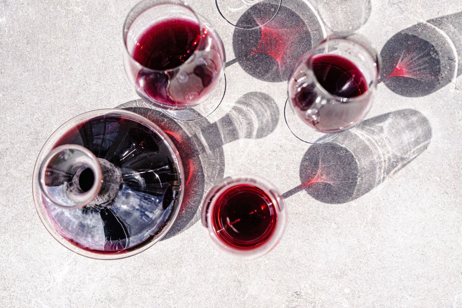 Overhead view of red wine glasses casting shadows on a light surface.