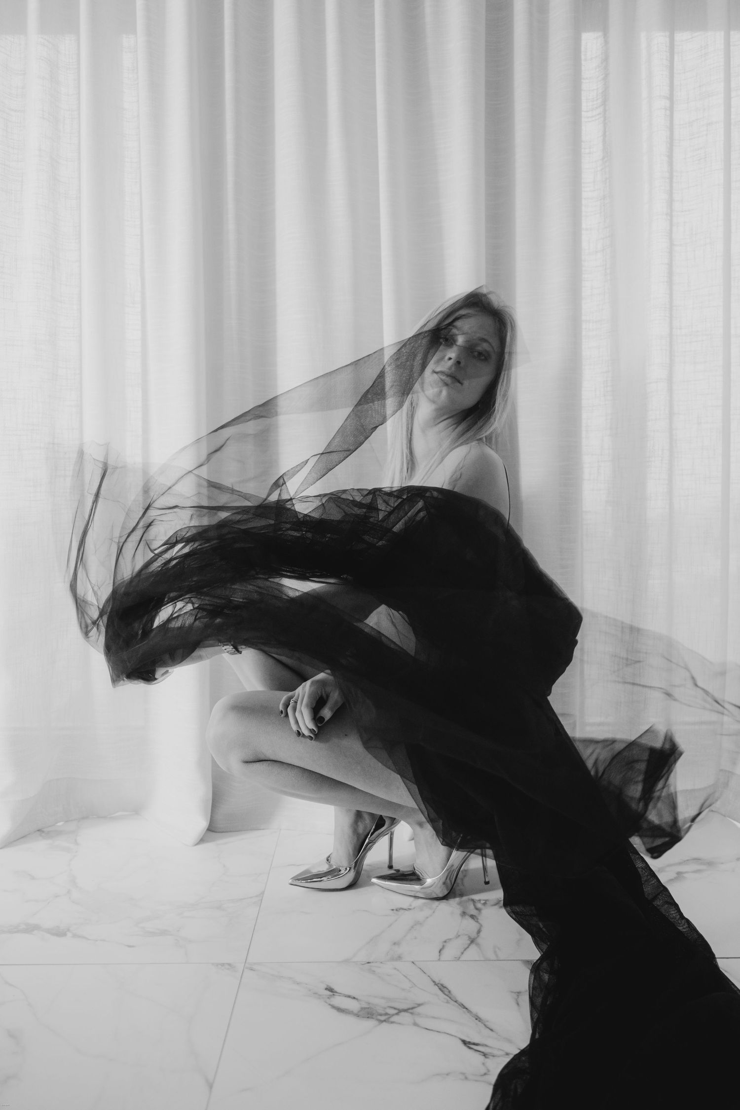 A figure in black flowing fabric creates a dramatic silhouette against white curtains in an artistic dance pose.