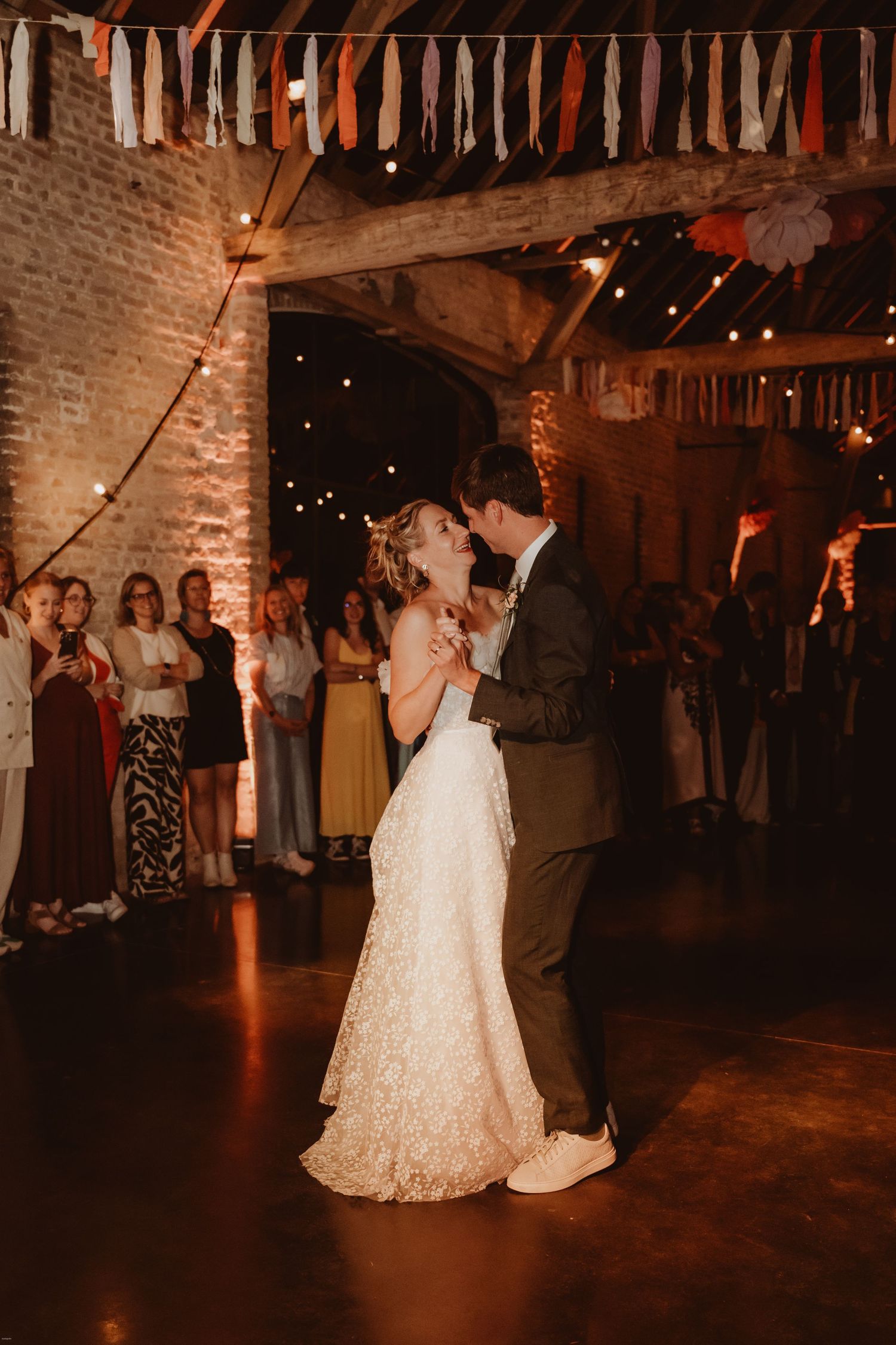 Couple shares their first dance under string lights in a rustic brick venue.