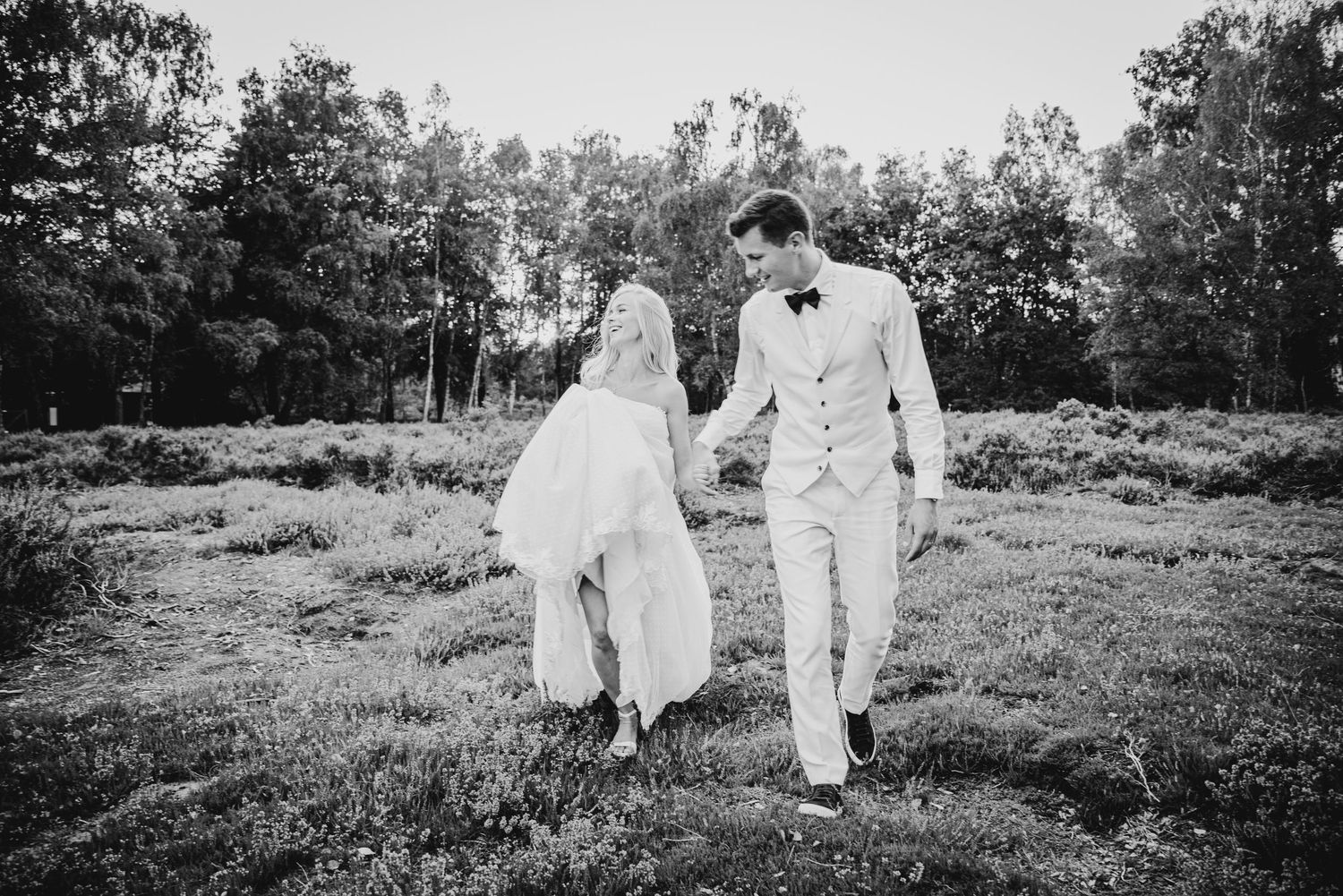 Black and white photo of newlyweds walking together in an outdoor field.