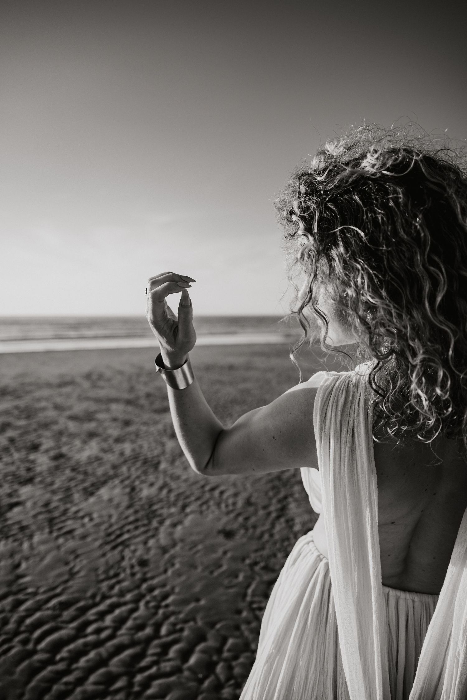 Black and white photo of figures in white dresses standing on a beach against a moody sky.