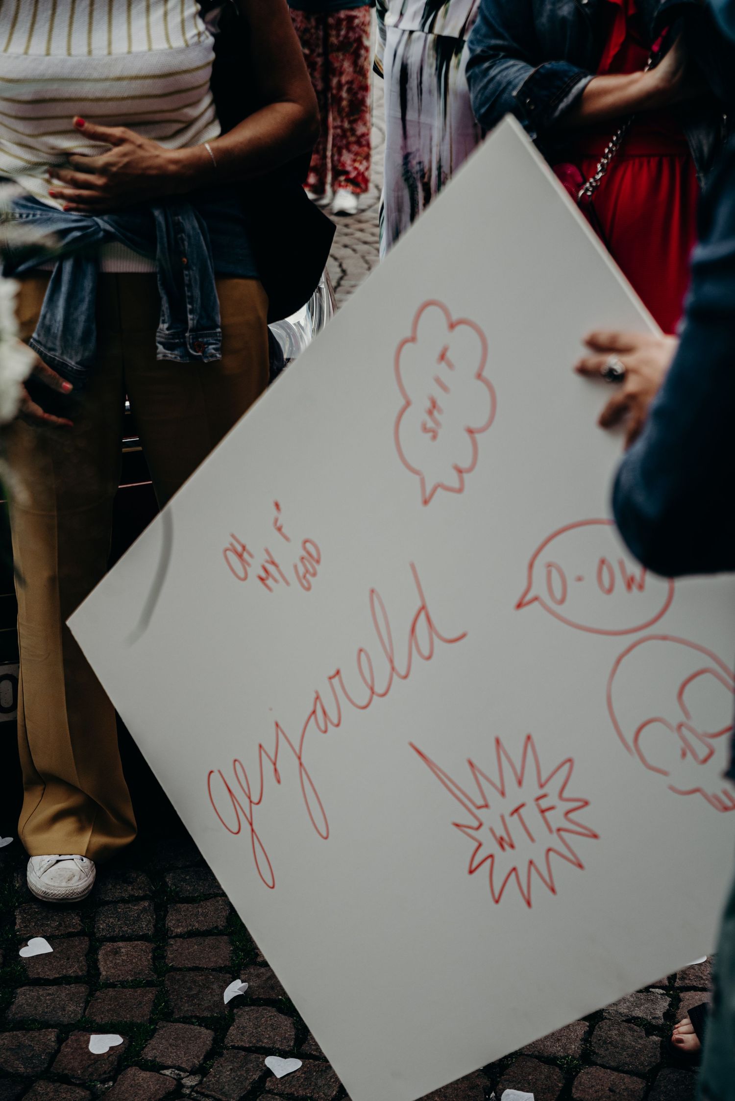 White paper signs with red handwritten messages displayed at an outdoor event.