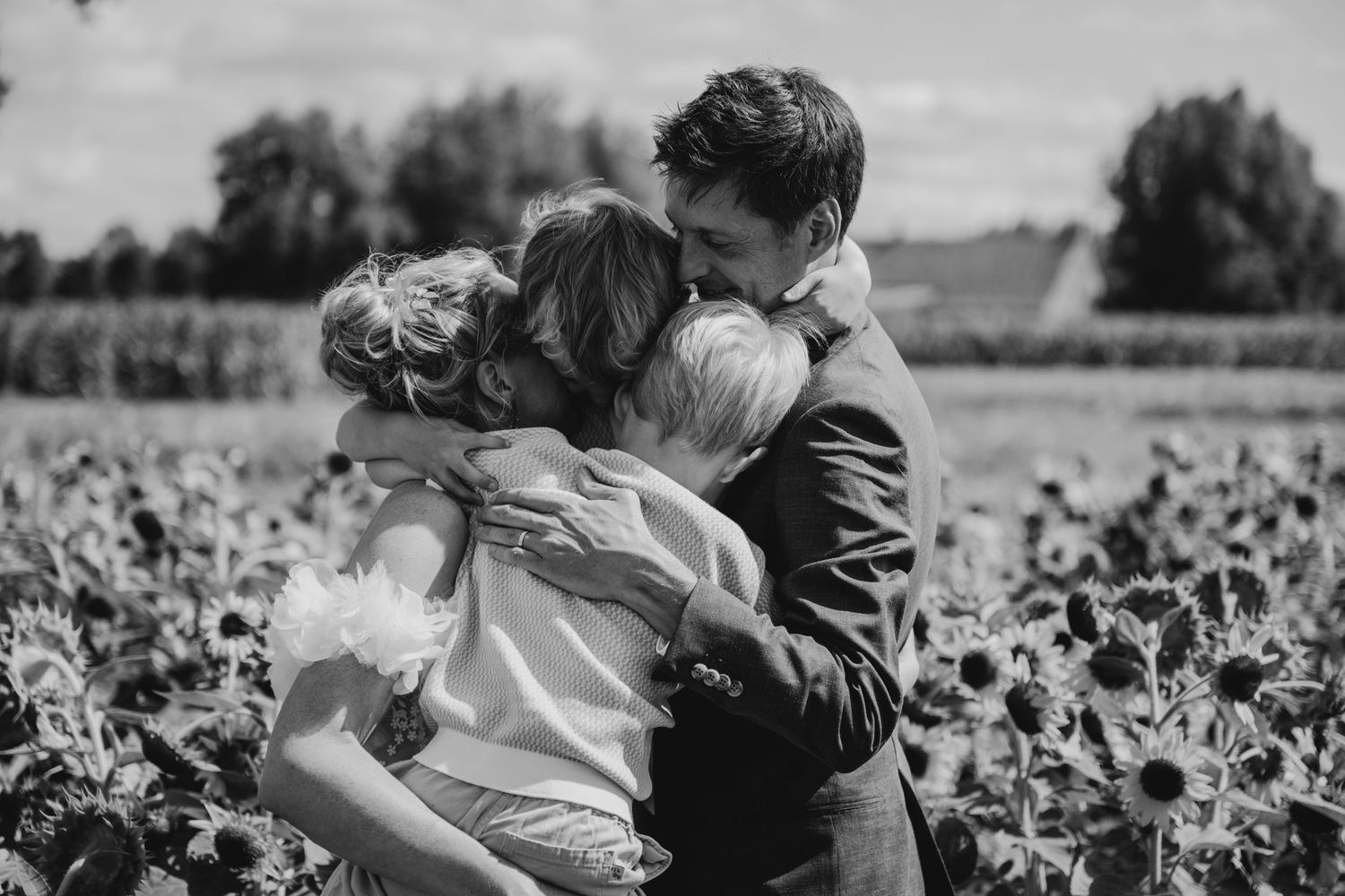 Couple embracing in a sunlit field with dramatic sky.