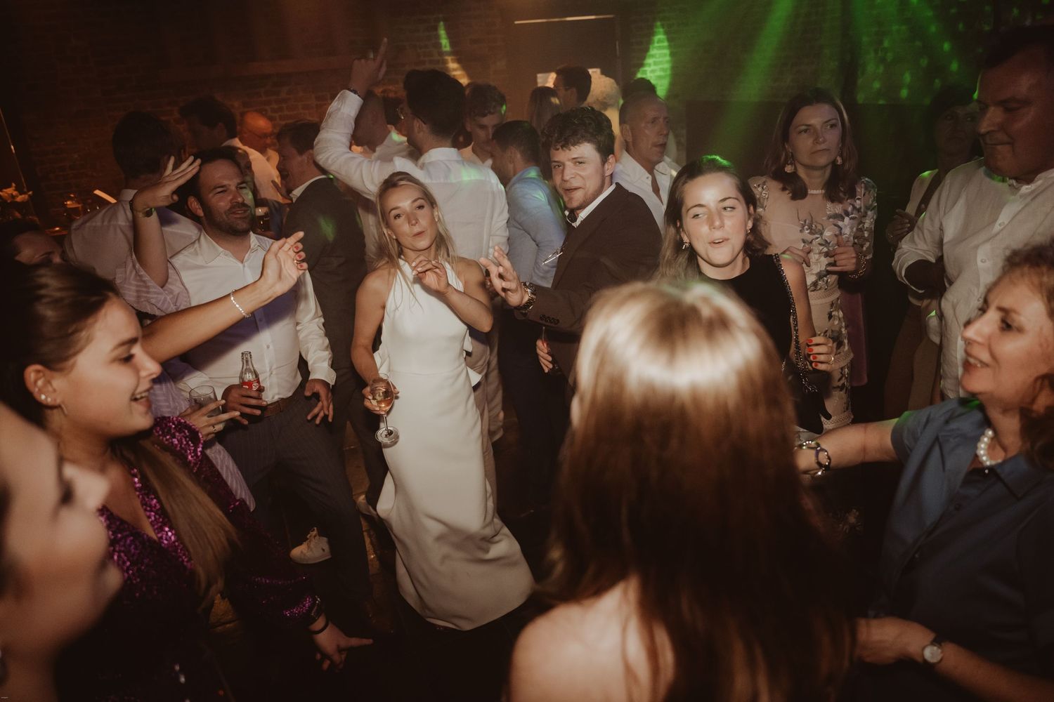 Energetic dance party scene with guests celebrating under green lighting effects.