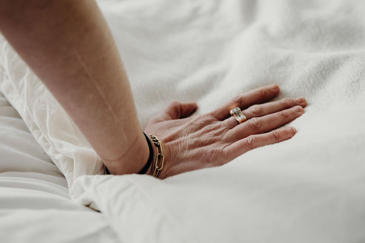Close-up of hands gently touching and intertwining on white bedding, showing intimacy and connection.