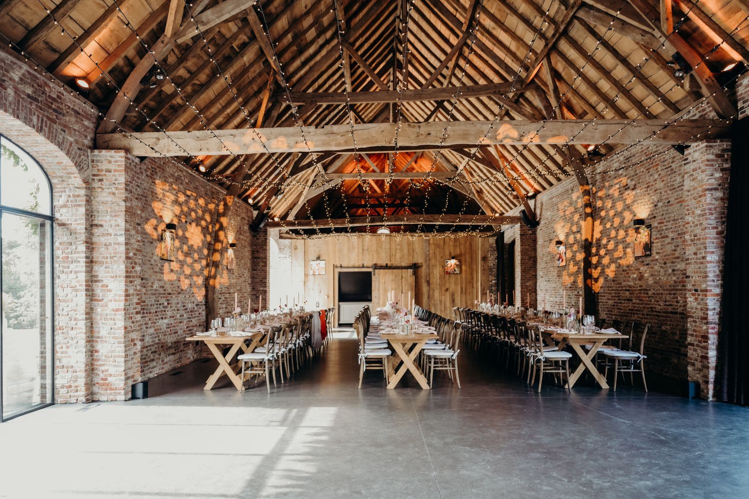 Rustic barn venue interior with exposed wooden beams and brick walls set up for an event.