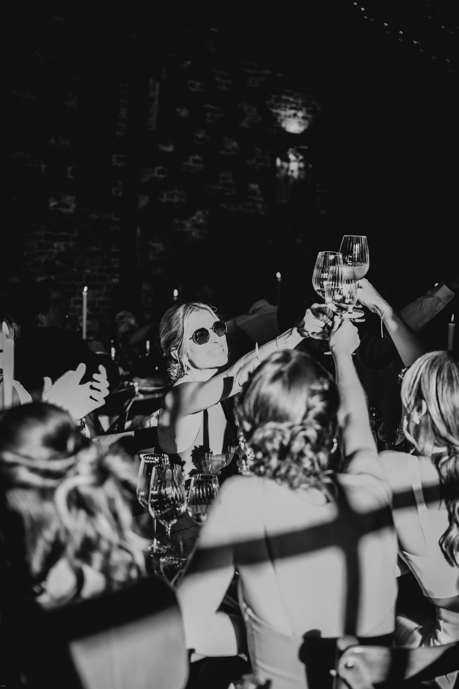 Black and white photo of wedding guests raising glasses during celebration.