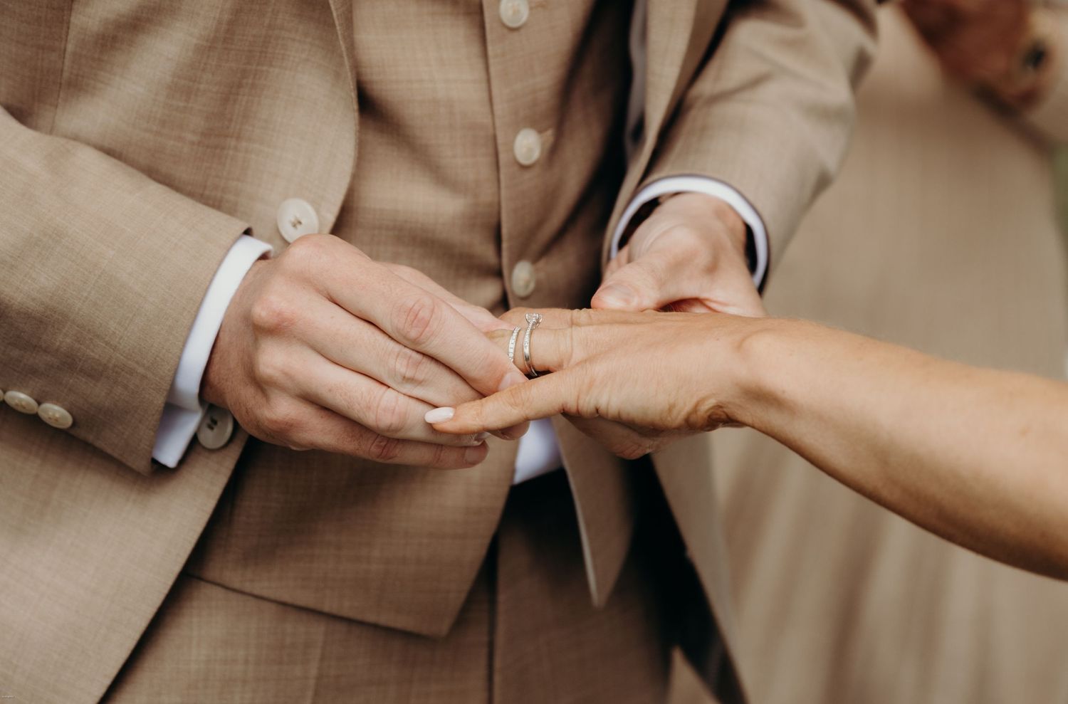 Close-up shot of hands exchanging wedding rings during ceremony.