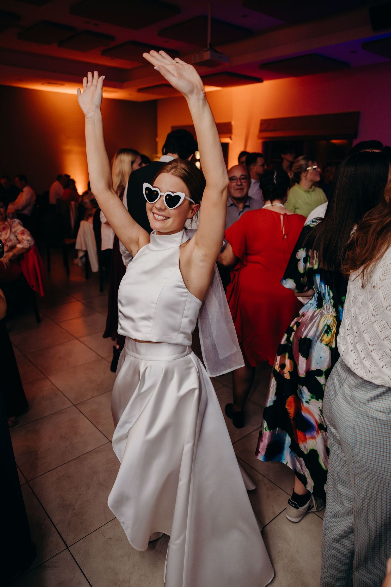 Wedding guests dancing and celebrating at a reception with colorful lighting.
