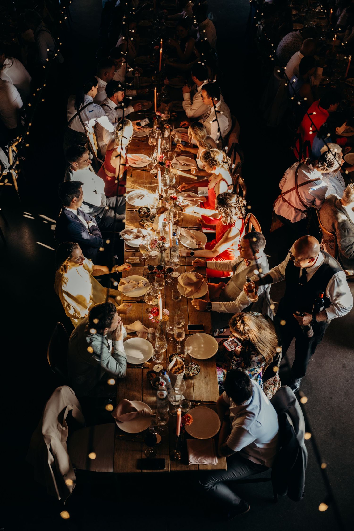 Overhead view of wedding dinner tables with candlelight and place settings in rustic venue.