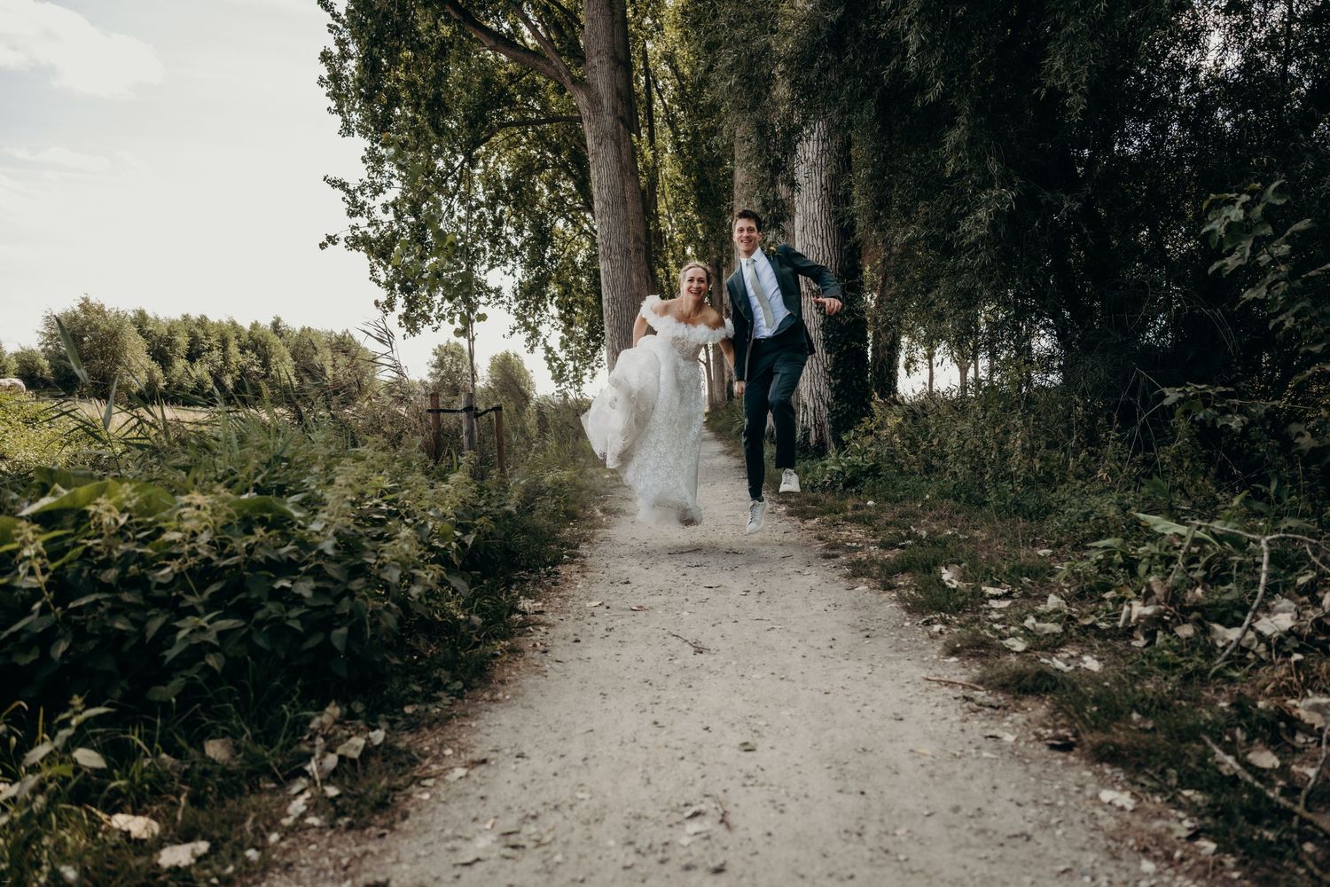 Couple in wedding attire walking along a sunlit forest path.