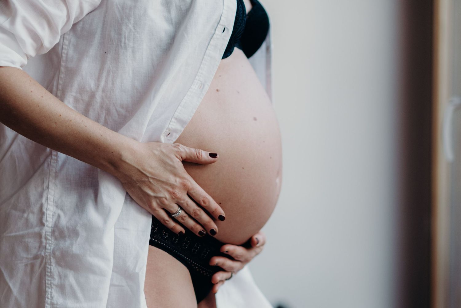 Silhouette of pregnant woman's belly against white backdrop with hands gently cradling the bump.
