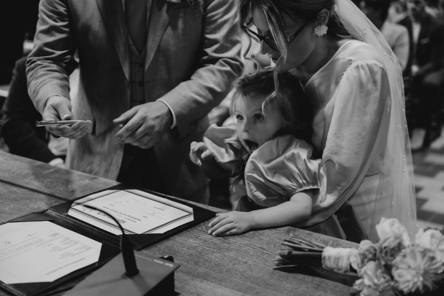 Wedding ceremony details showing hands signing documents in black and white.