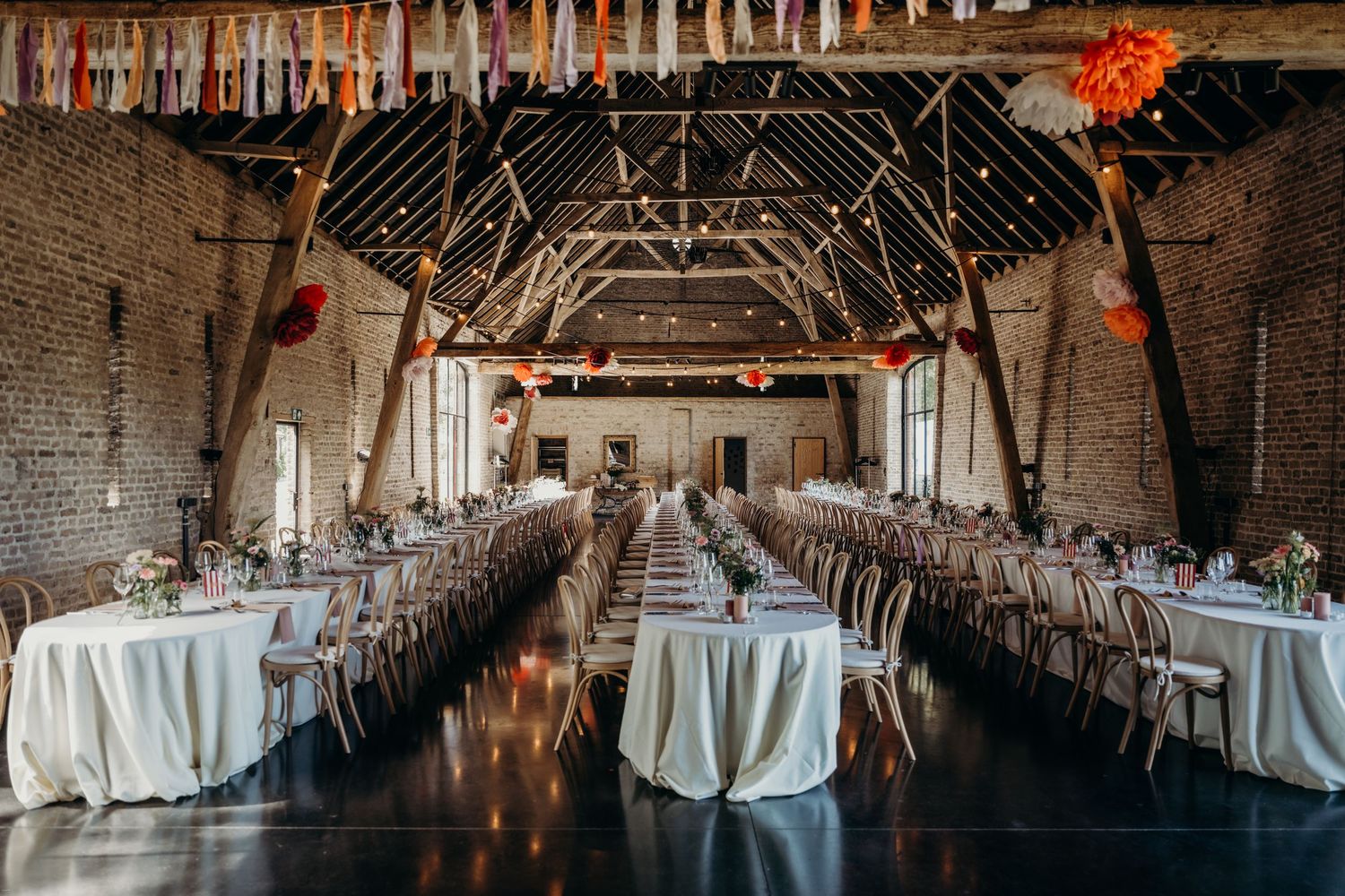 Rustic barn wedding venue with exposed beams and elegant table settings in a long hall.