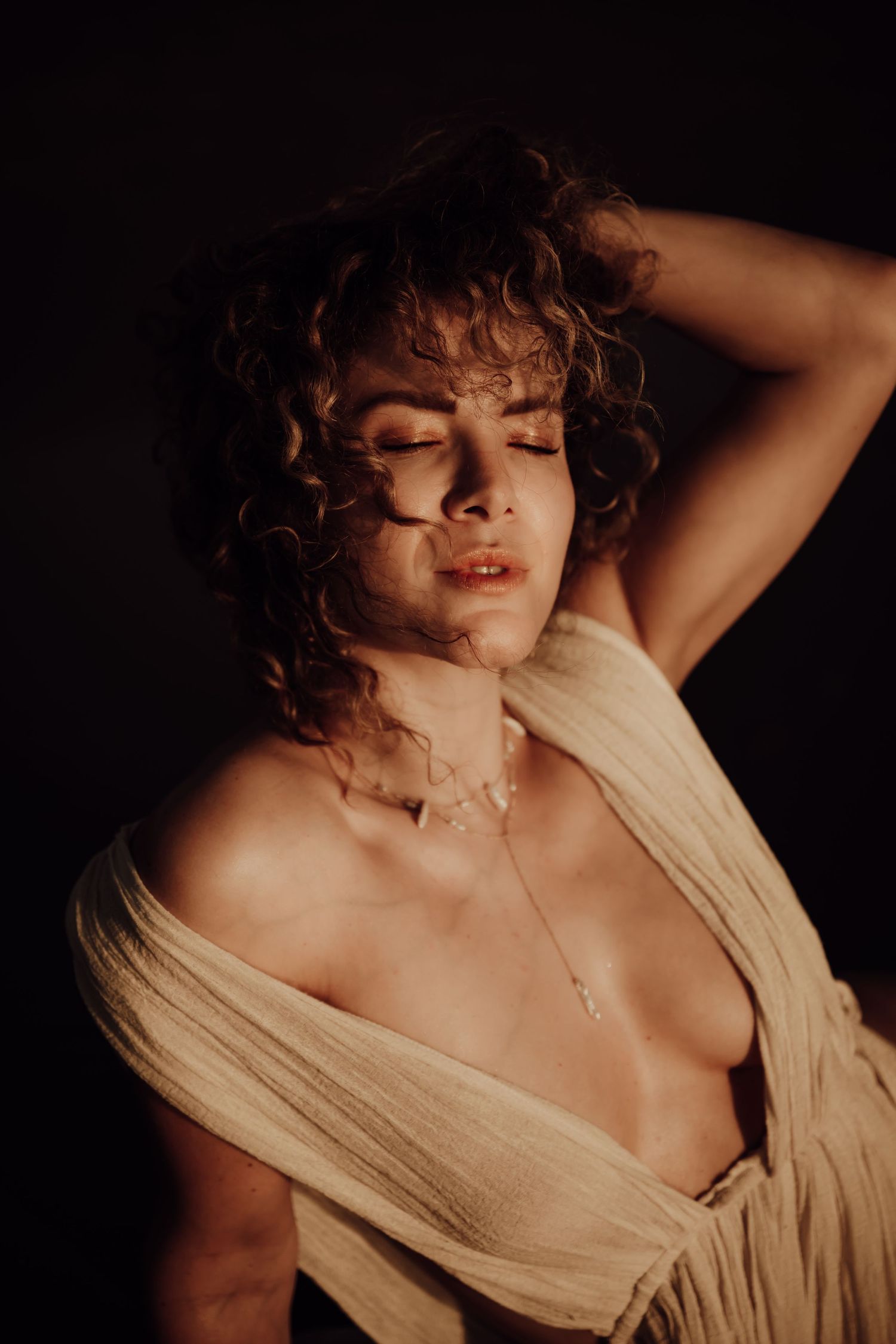 Artistic portrait series showing a person with curly hair in cream-colored fabric against dark background.