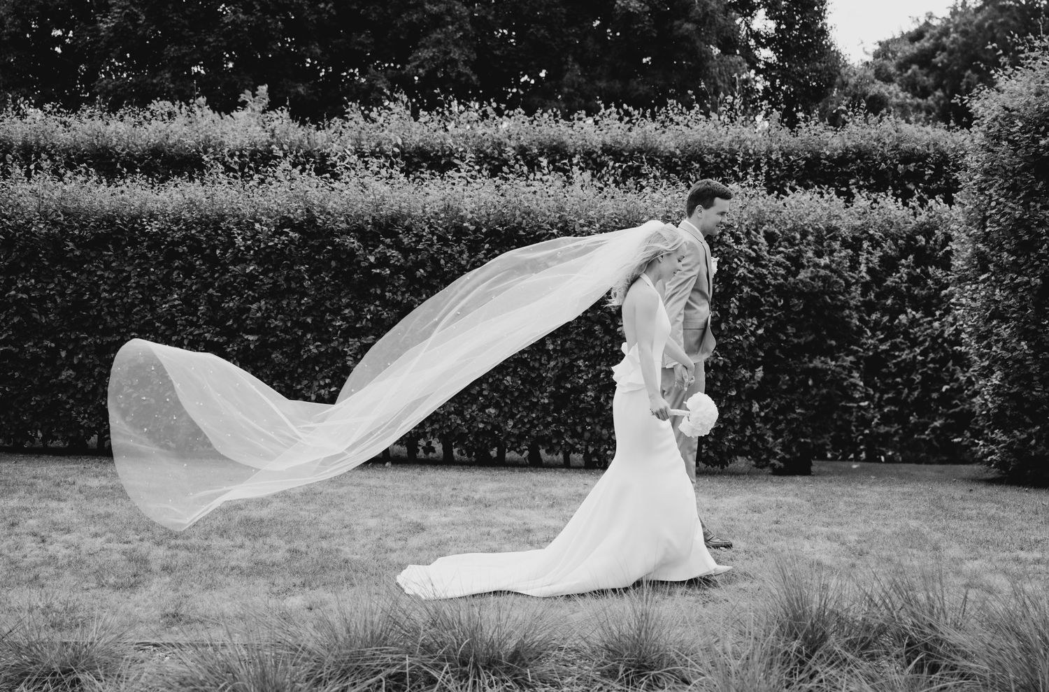 Flowing white wedding dress veil caught in the wind across a green field.