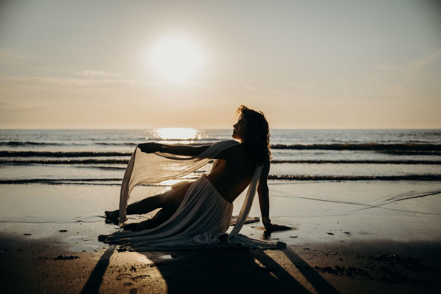 Silhouetted figures on a beach at sunset with long shadows stretching across the sand.