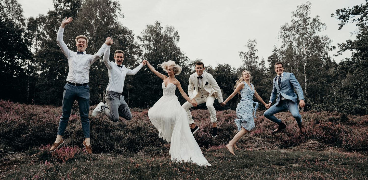 Wedding celebration group photo with people jumping outdoors.